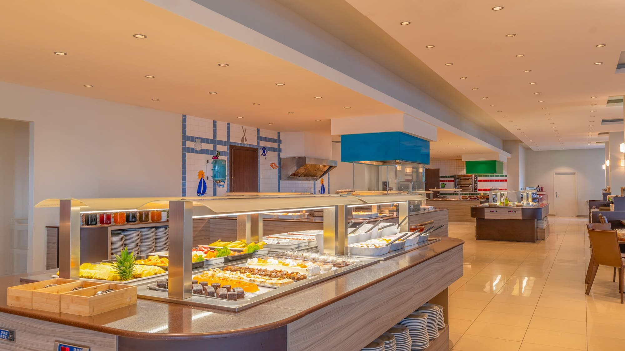 Bright hotel dining buffet featuring fresh food, fruits, and varied desserts.