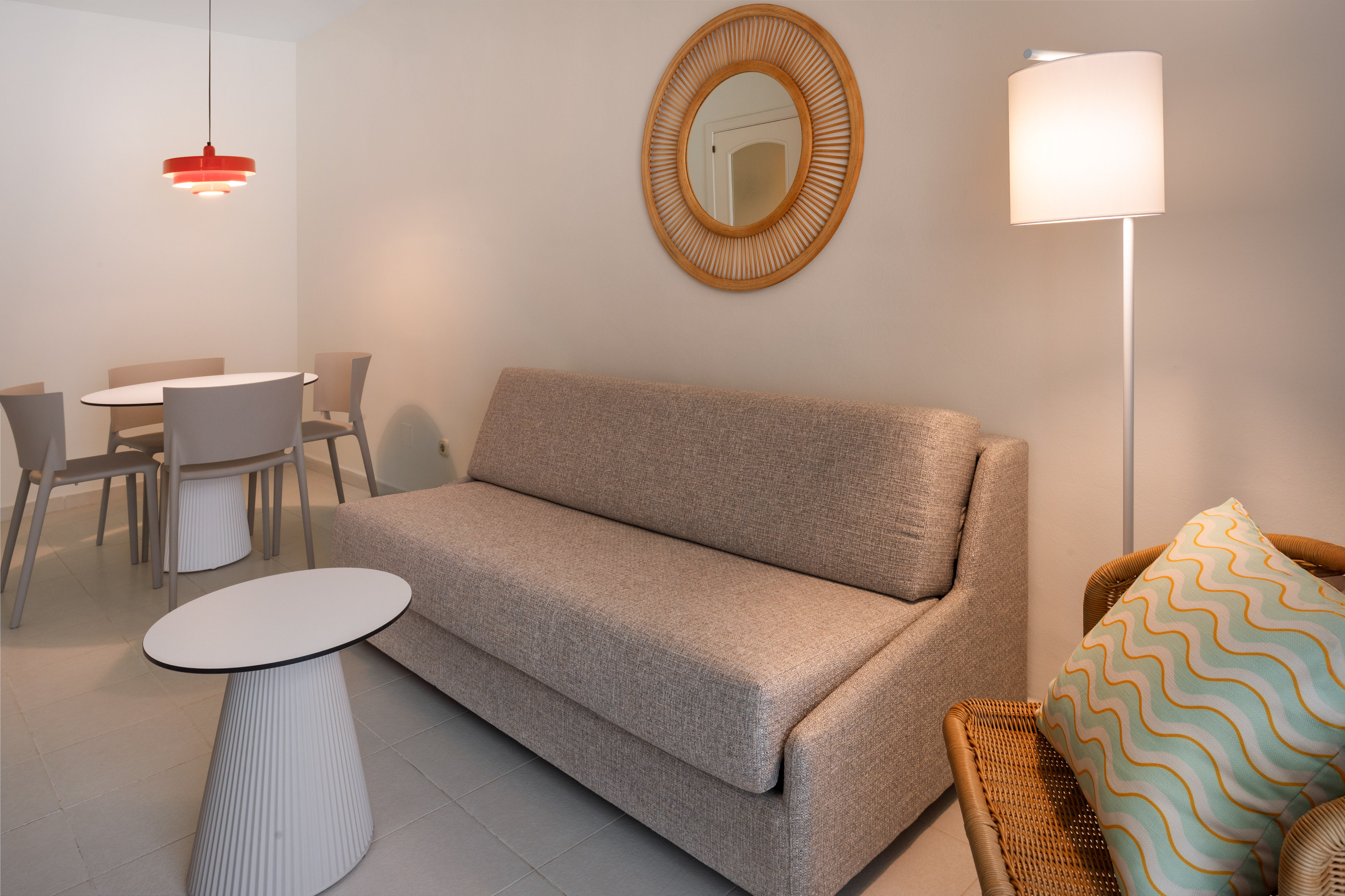 Modern living area with sofa, dining set, floor lamp, and rattan mirror.
