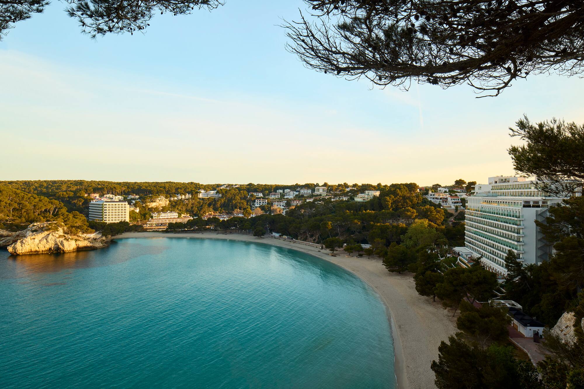 Turquoise bay with sandy beach, green hills, and coastal resort hotels.