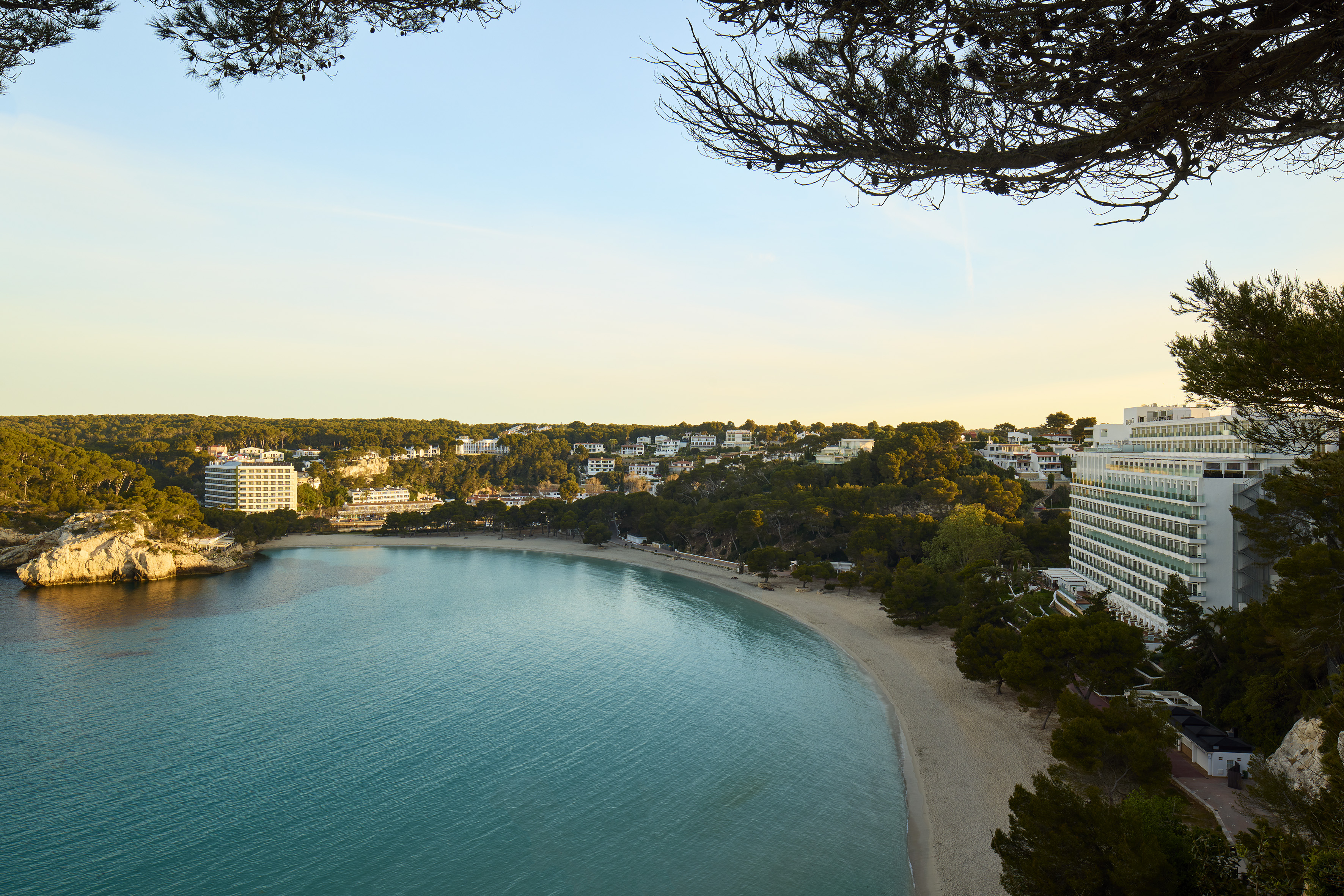 Turquoise bay with sandy beach, green hills, and coastal resort hotels.