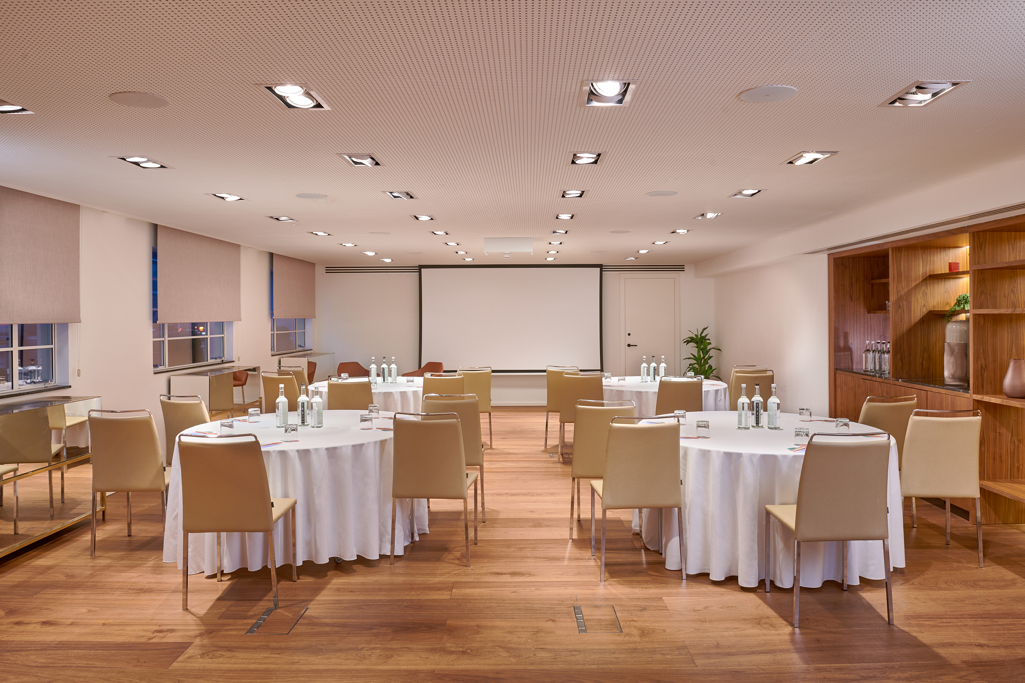 Modern conference room with round tables, beige chairs, and projection screen.