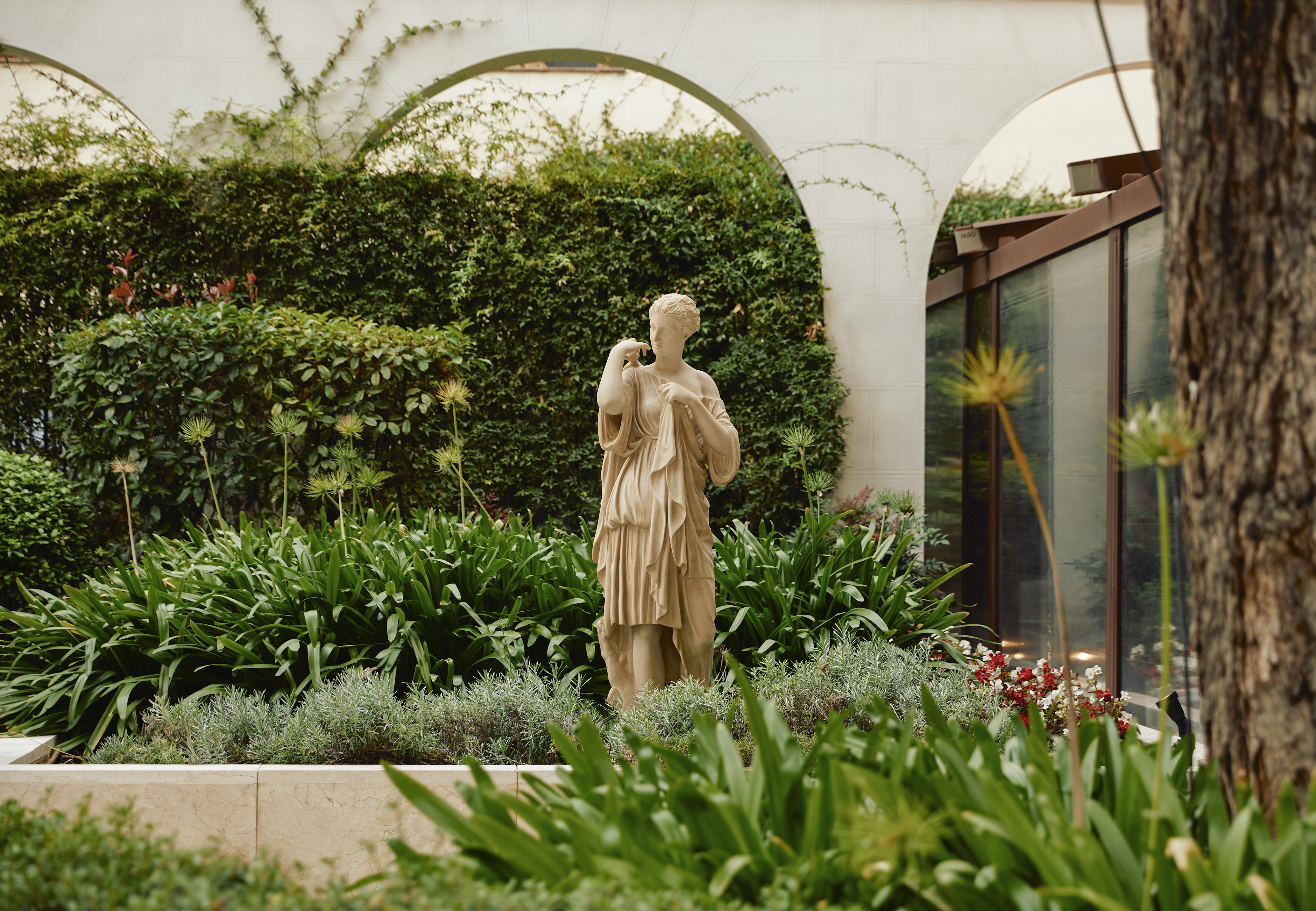 Classical female statue in a lush green garden with architectural arches.