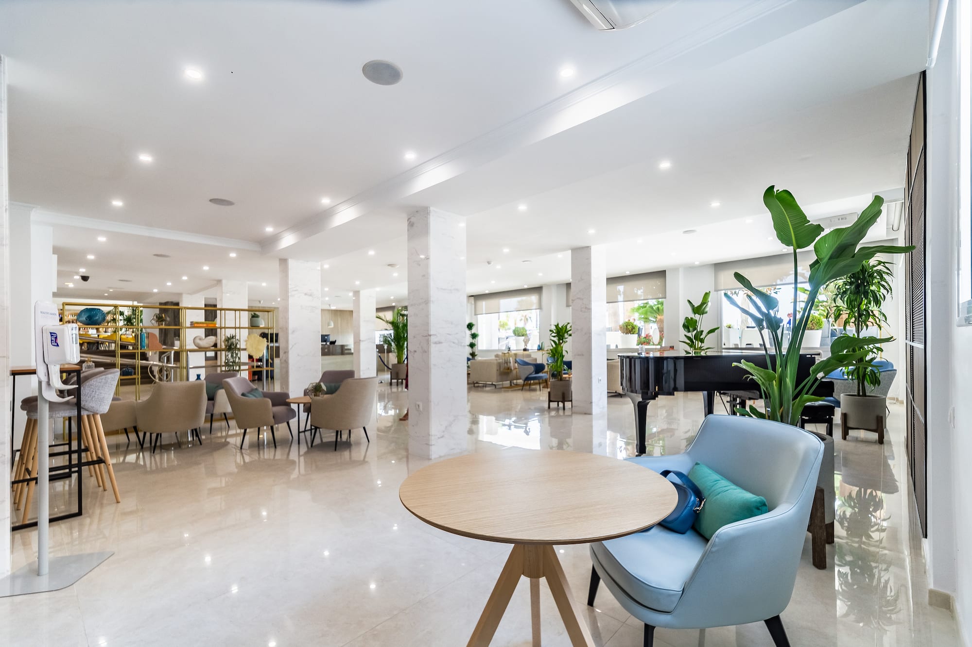 Bright, modern hotel lobby lounge with various seating, piano, and marble floor.