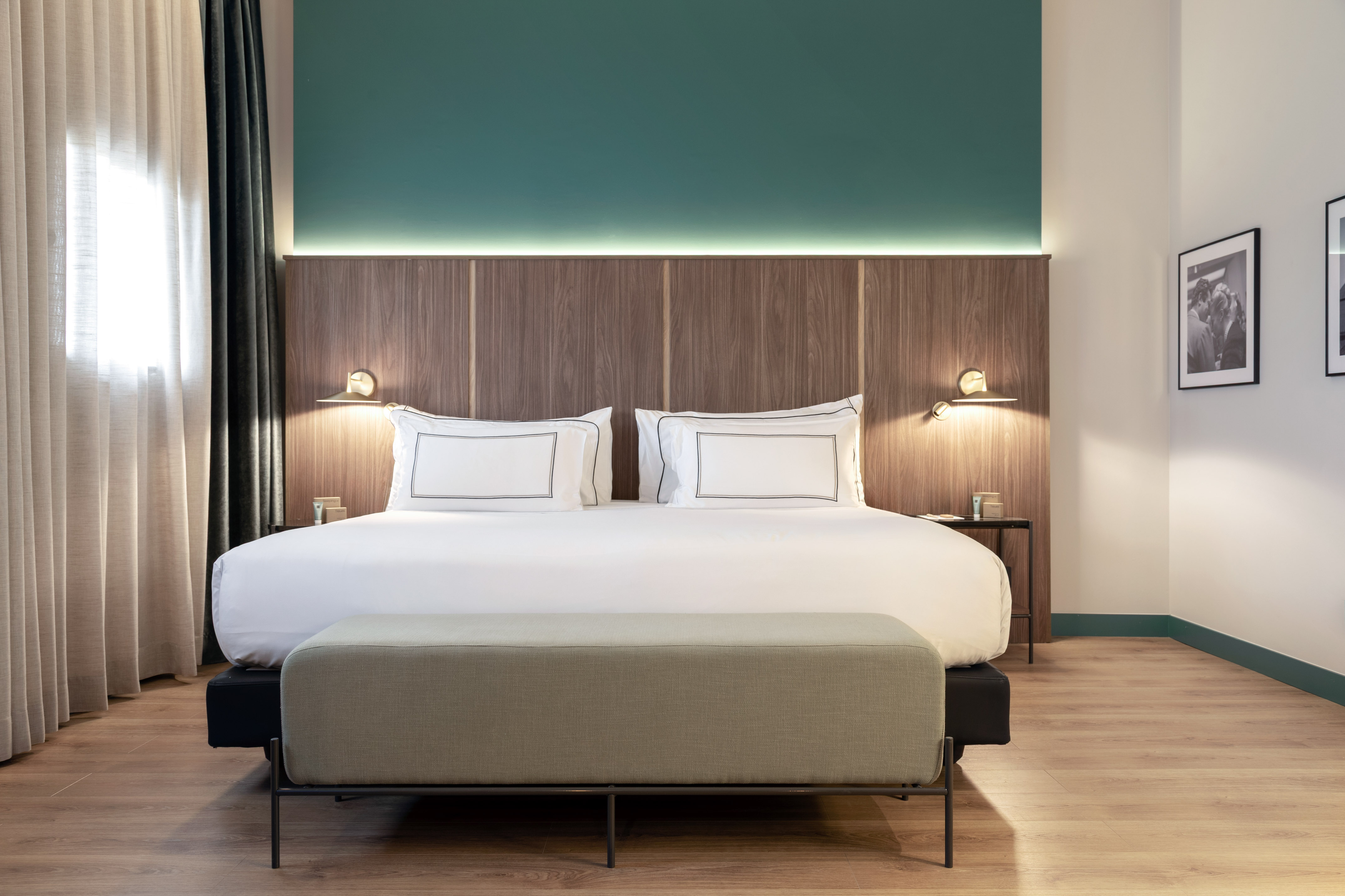 Modern hotel bedroom with king bed, wooden headboard, and teal accent wall.