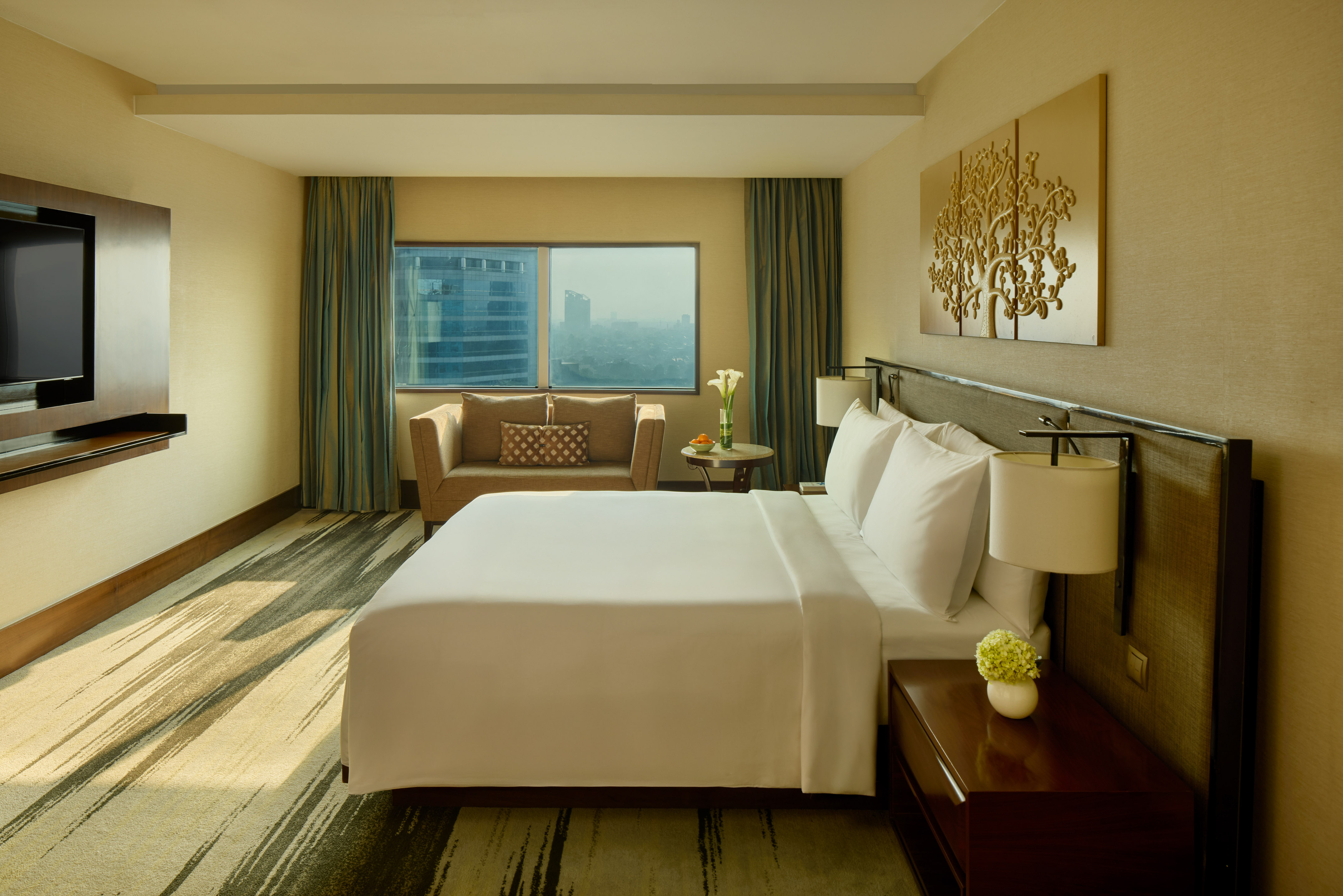 Modern hotel room with king bed, sofa, city view, and stylish decor.