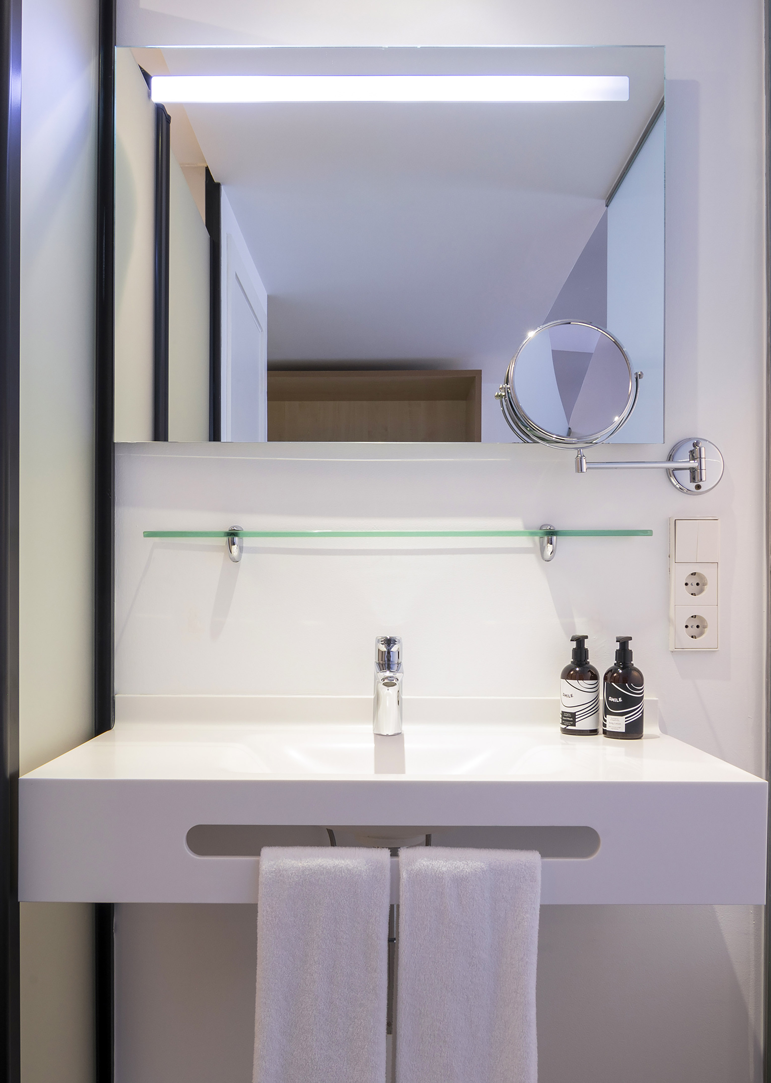 Modern white bathroom vanity with sink, illuminated mirror, and towels.