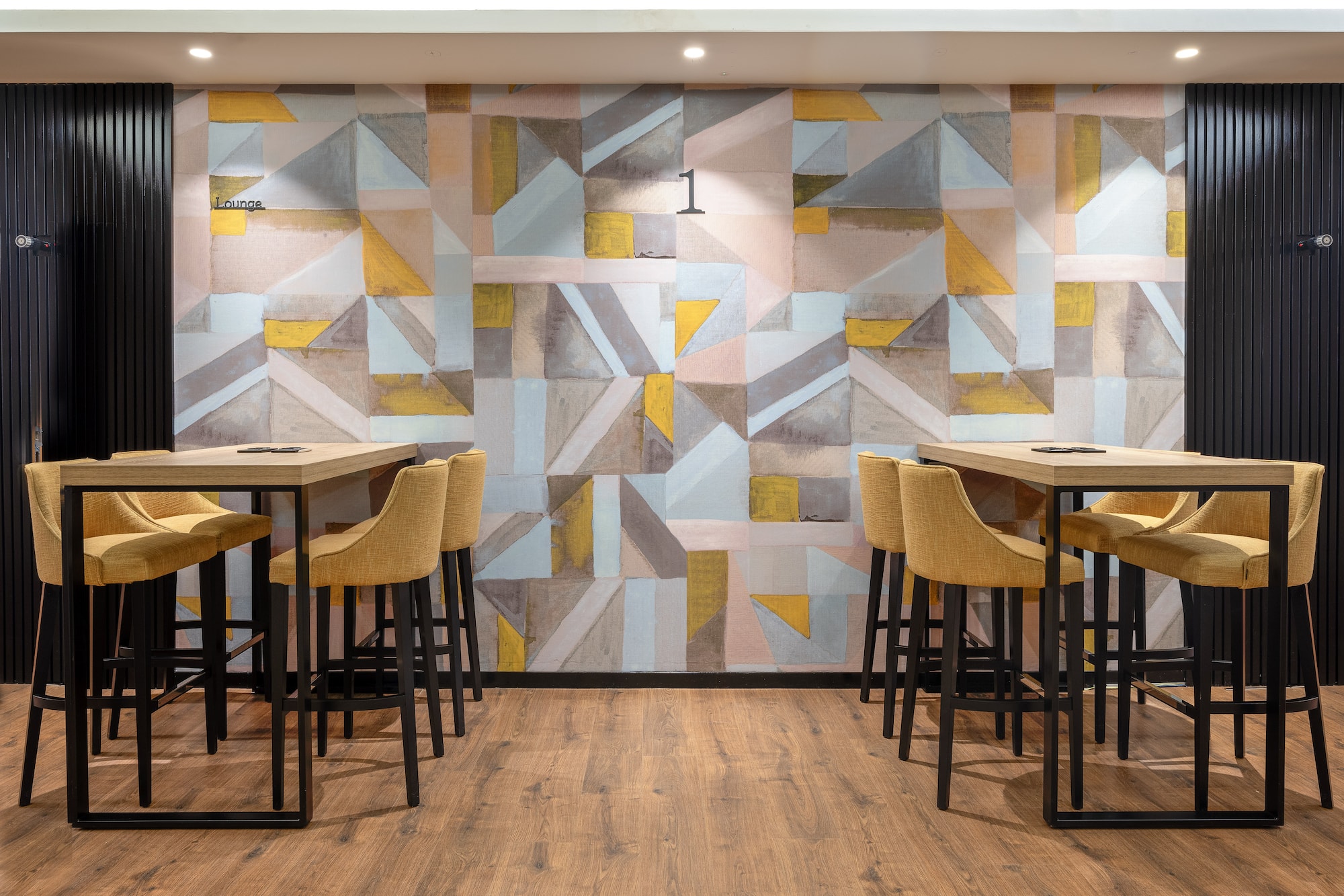 Modern lounge with yellow bar stools, high tables, geometric wallpaper, and wood floor.