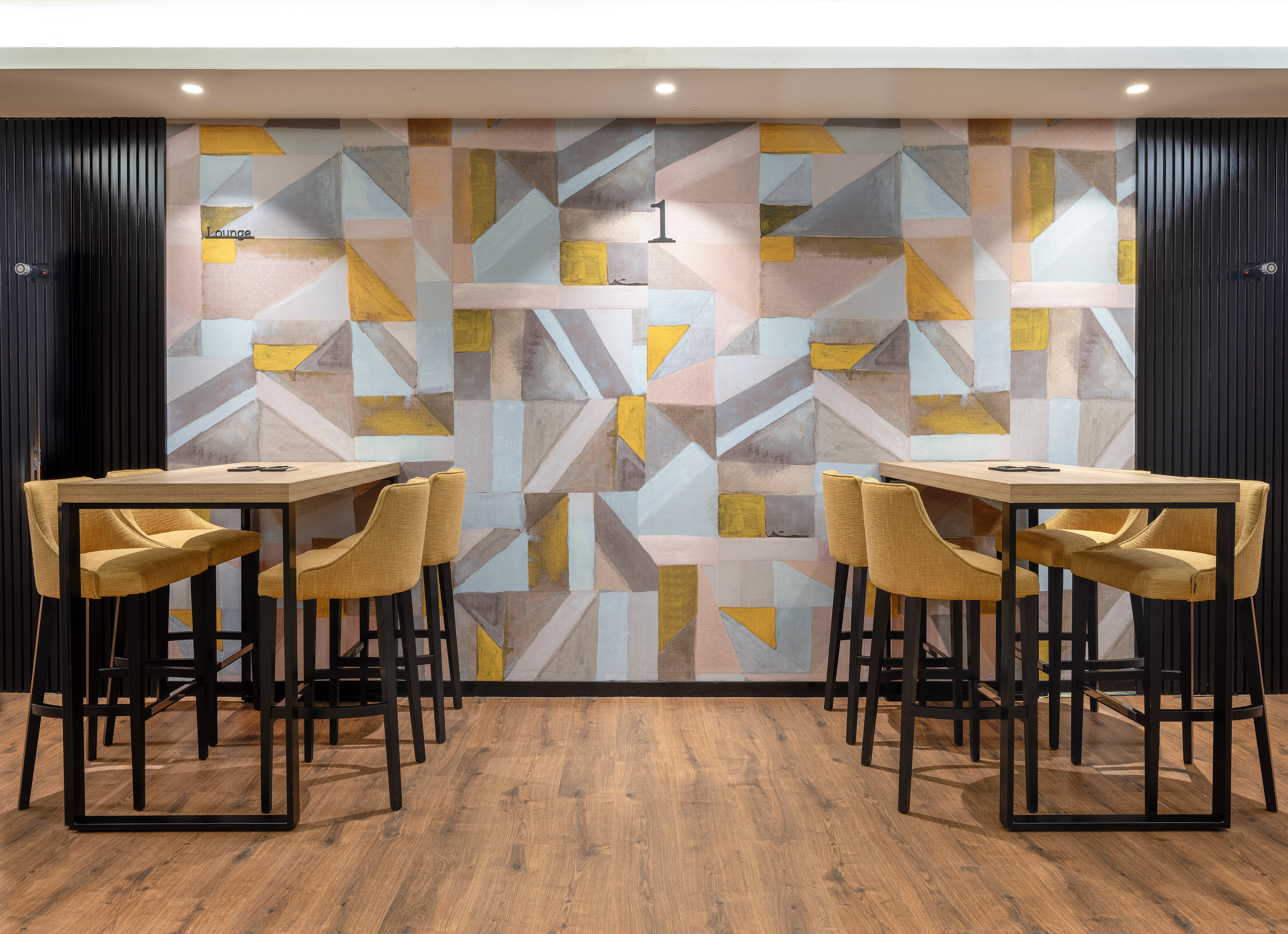 Modern lounge with yellow bar stools, high tables, geometric wallpaper, and wood floor.