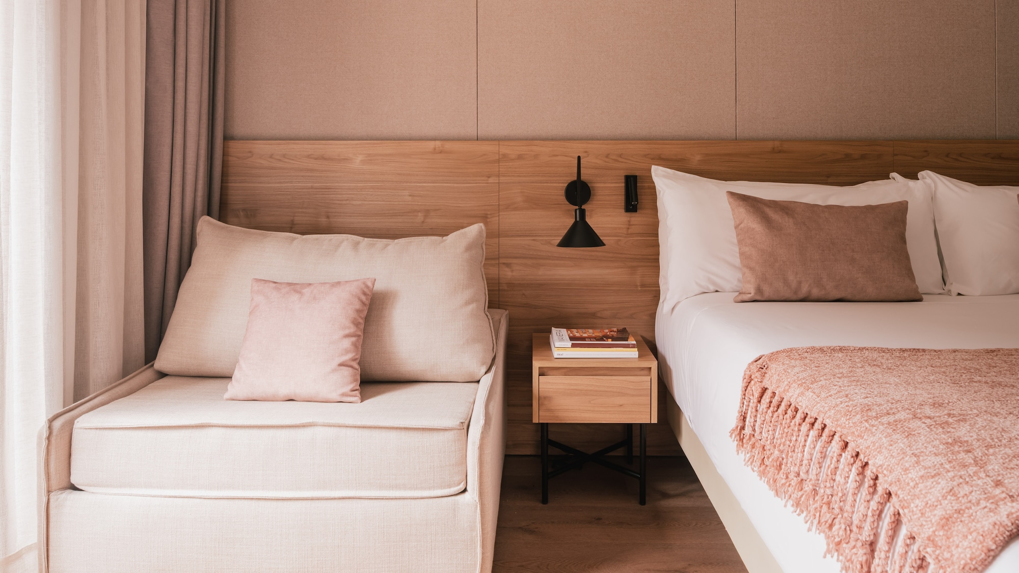 Modern bedroom with bed, chaise lounge, wooden headboard, and pink accents.