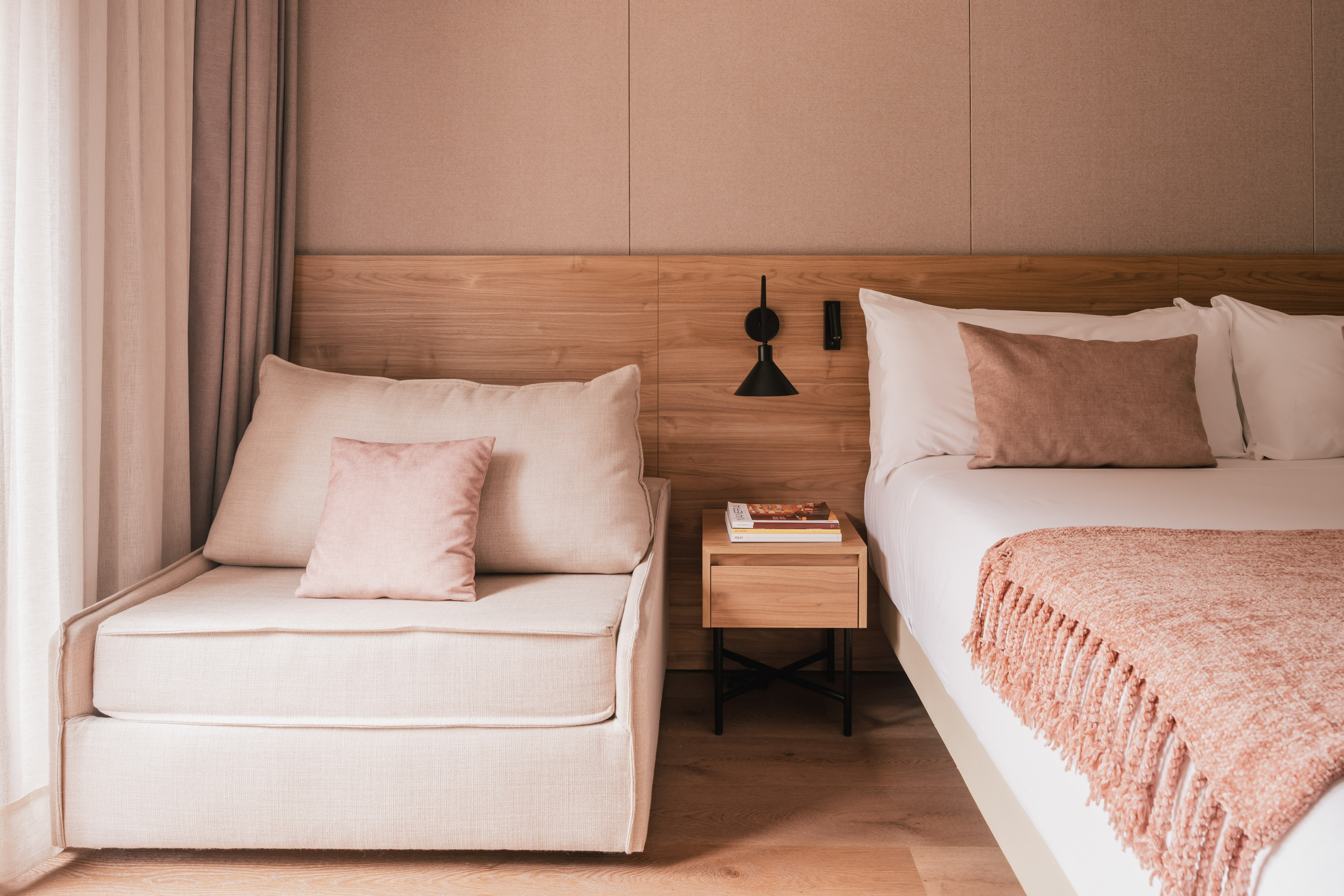 Modern bedroom with bed, chaise lounge, wooden headboard, and pink accents.