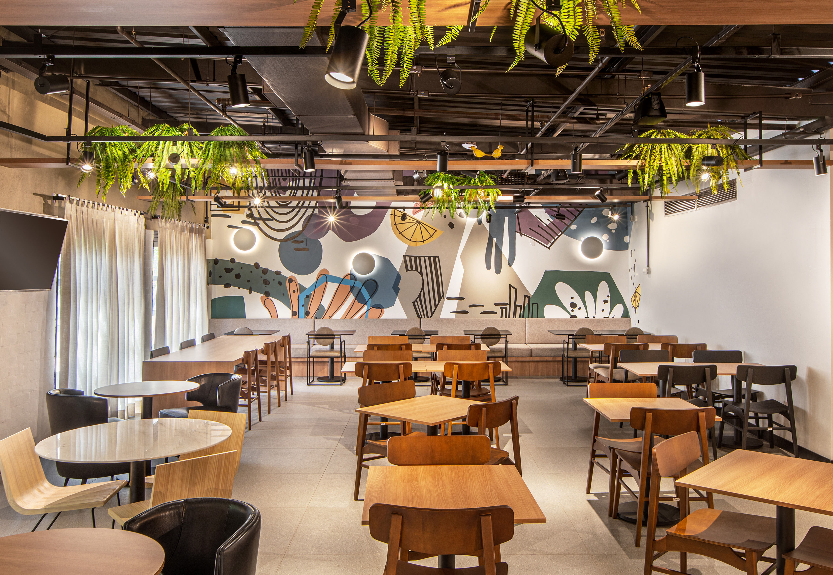 Modern cafe interior with wood tables, abstract wall art, and hanging ferns.