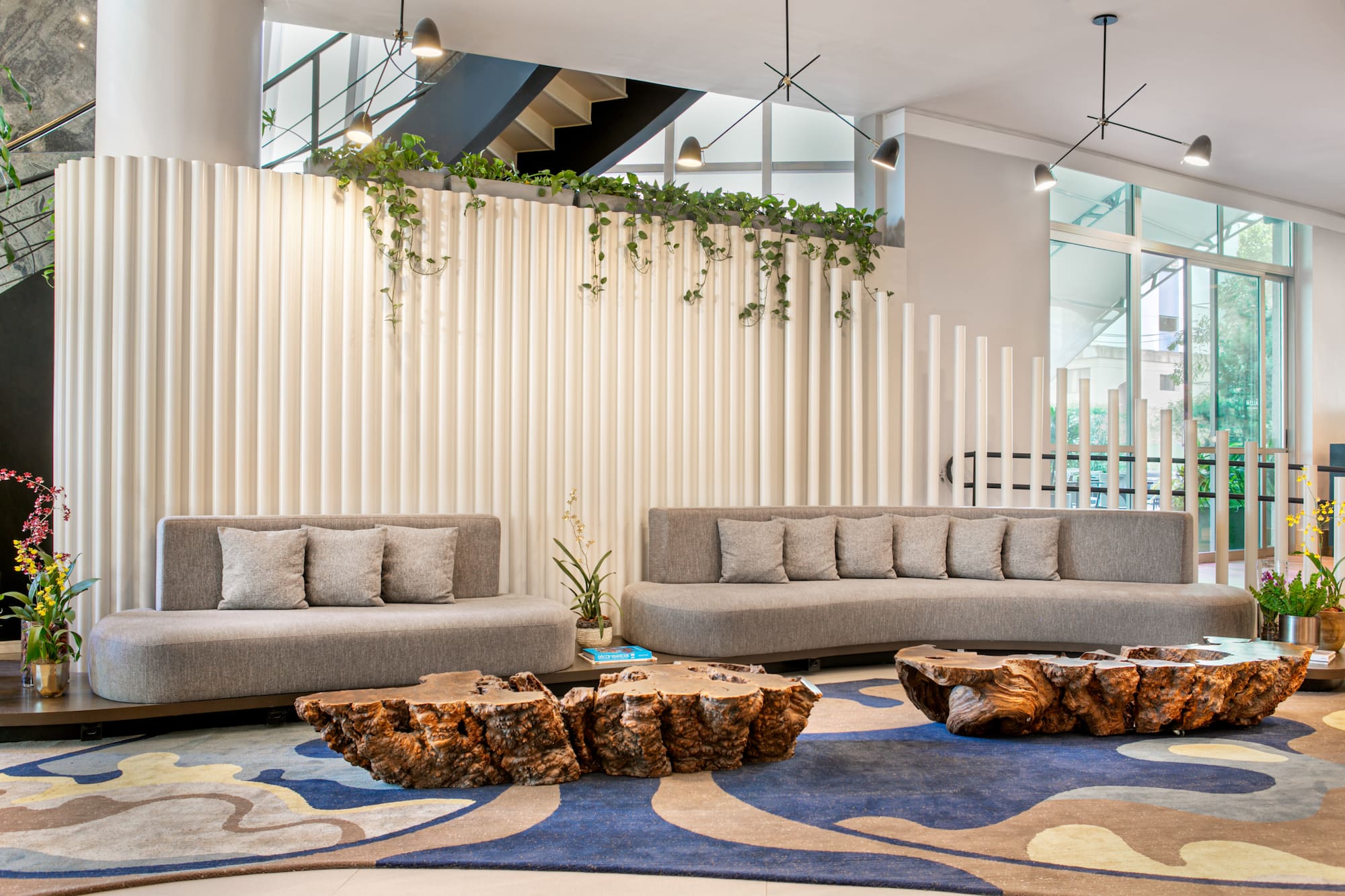 Modern lounge with grey sofas, natural wood tables, ribbed wall, and plants.