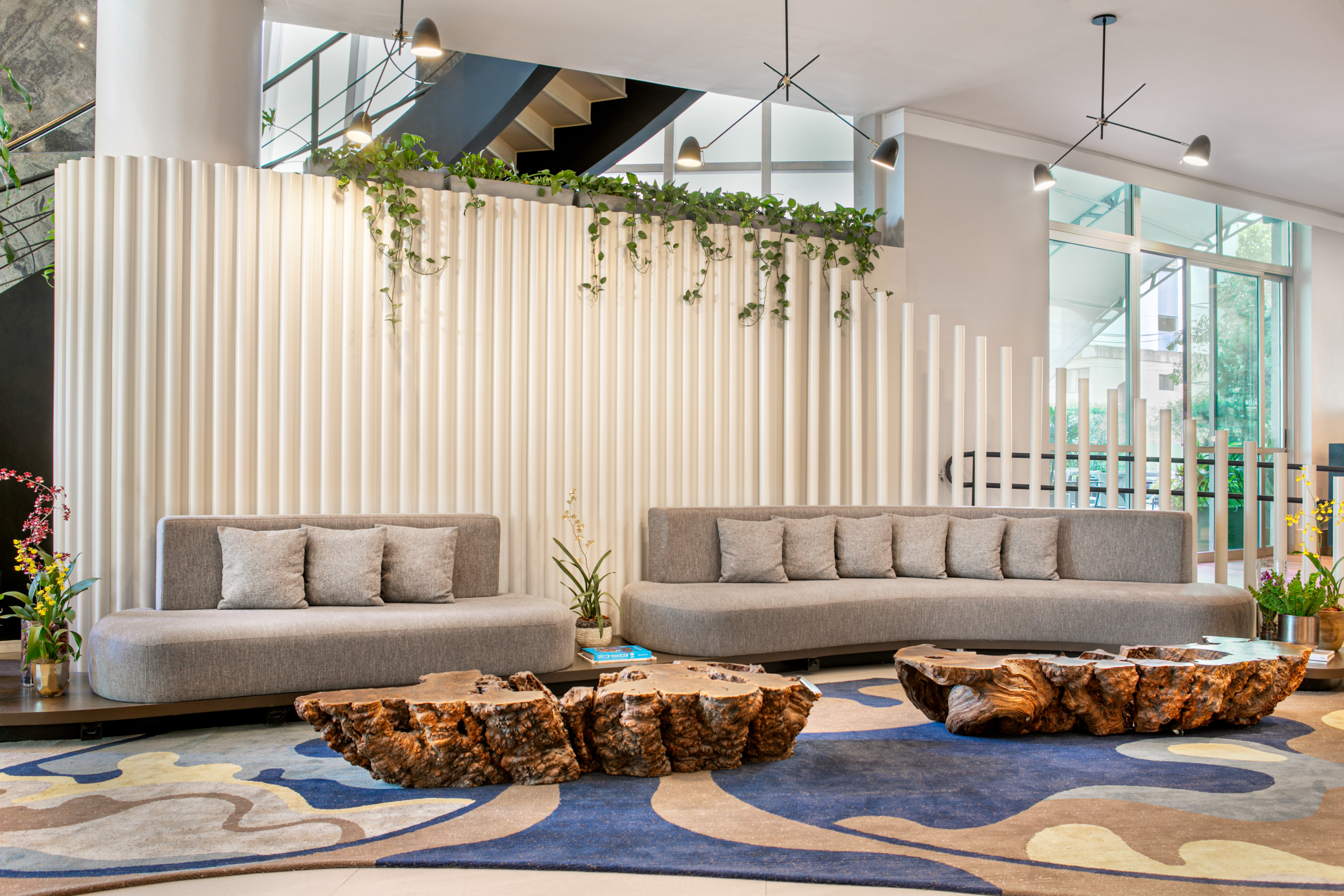 Modern lounge with grey sofas, natural wood tables, ribbed wall, and plants.