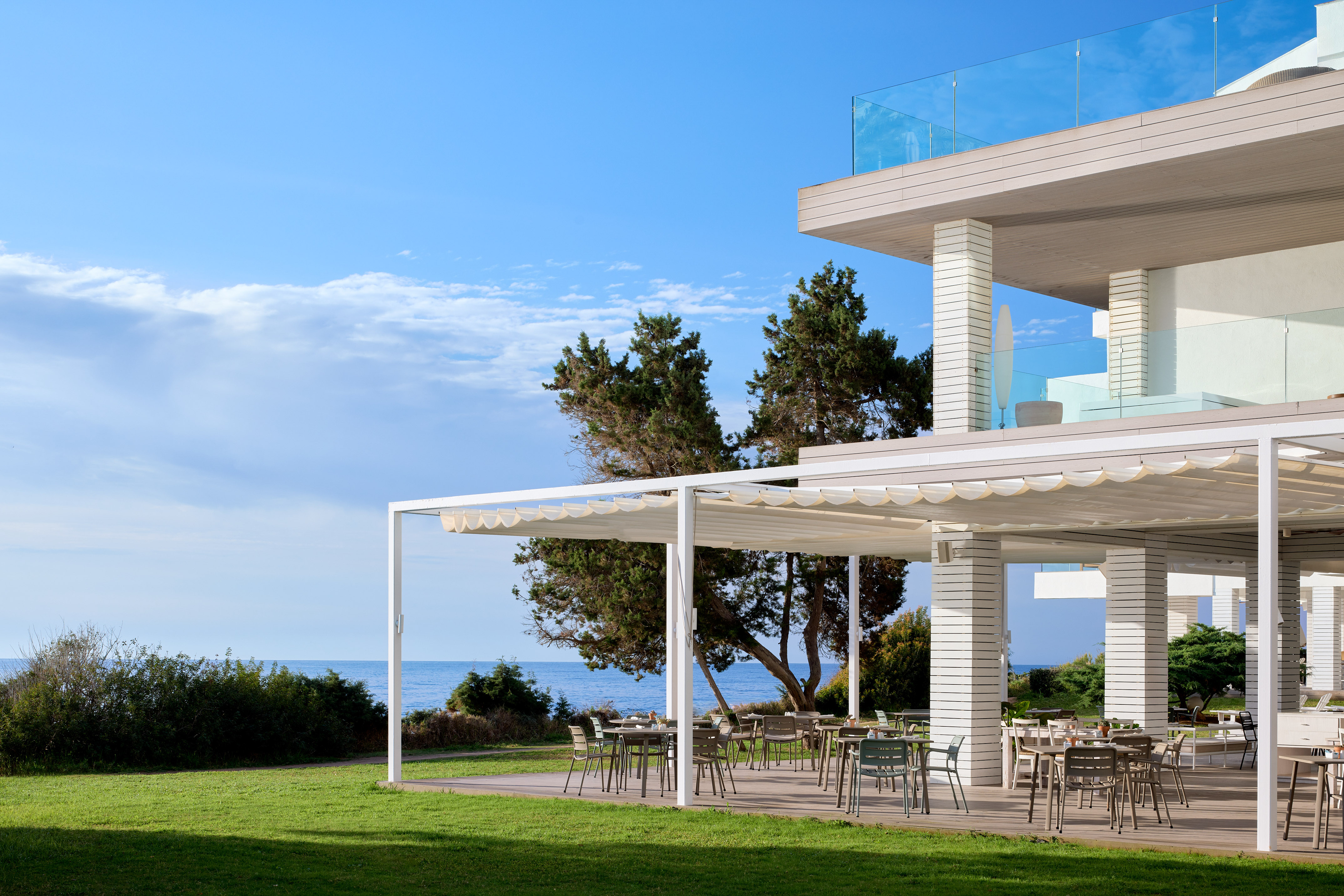Shaded outdoor restaurant patio at modern coastal resort with sea view.