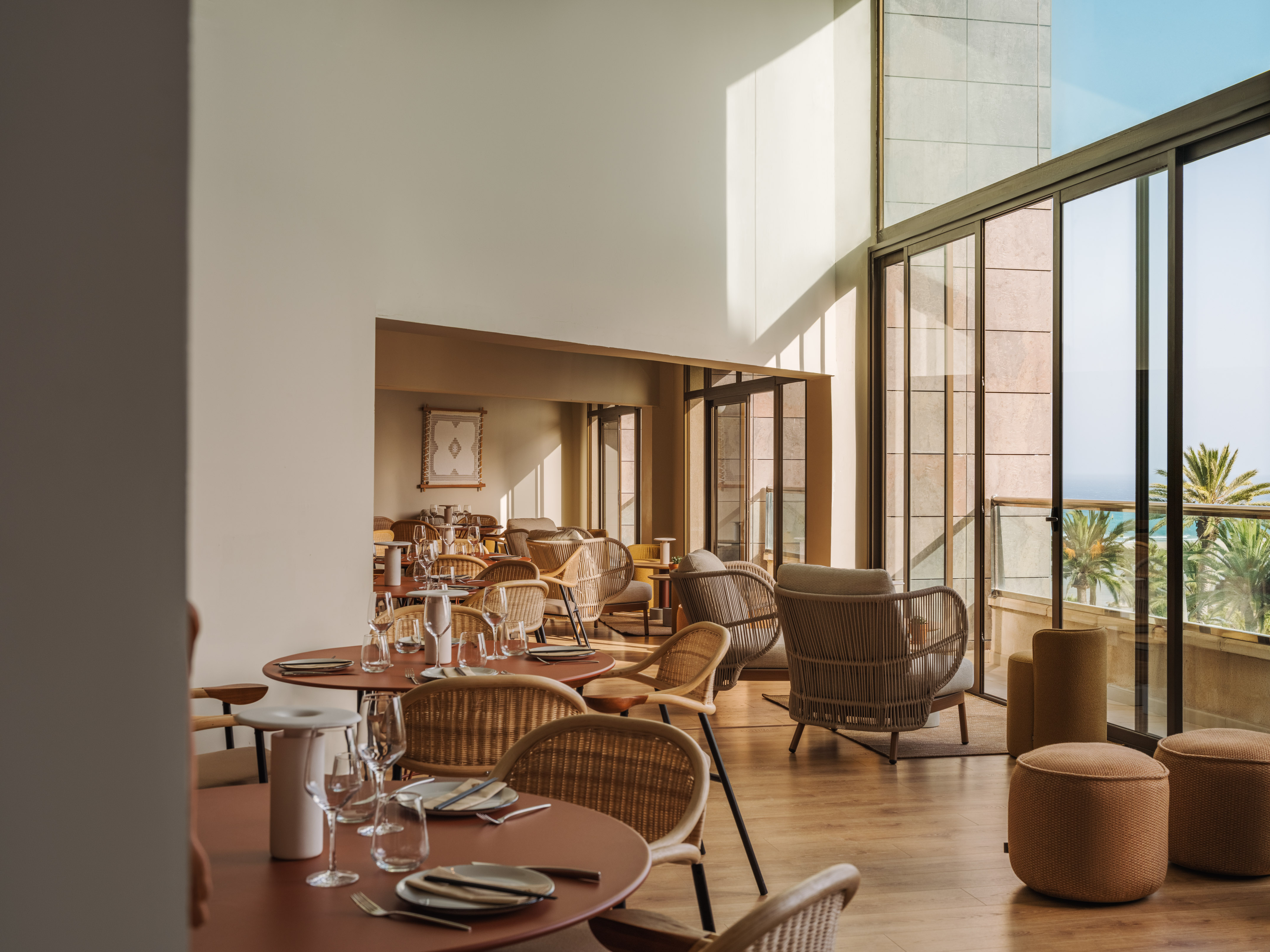 Modern restaurant lounge with wicker furniture, dining tables, and ocean view.