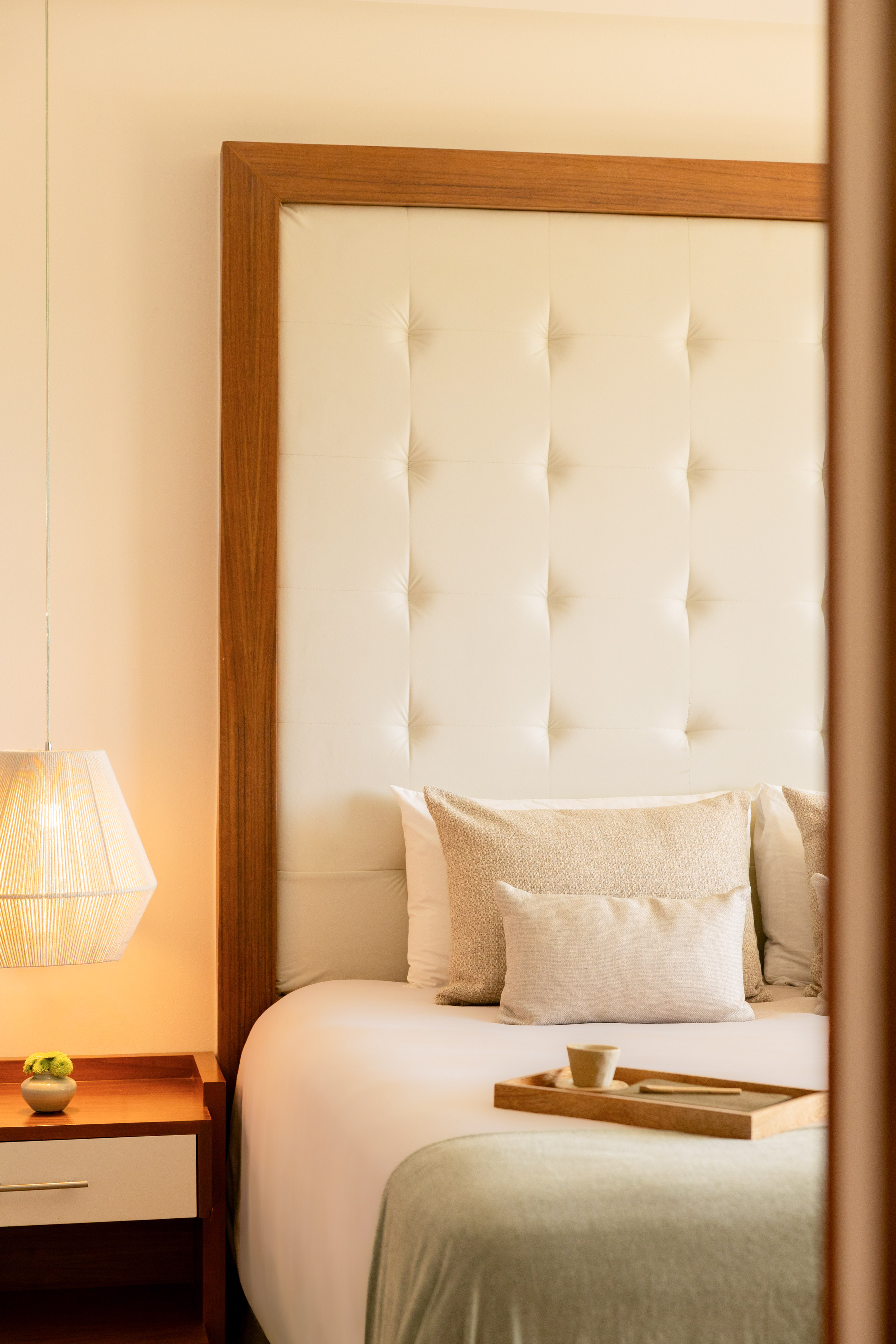 Cozy bedroom with cream tufted headboard, bedside lamp, and bed tray.