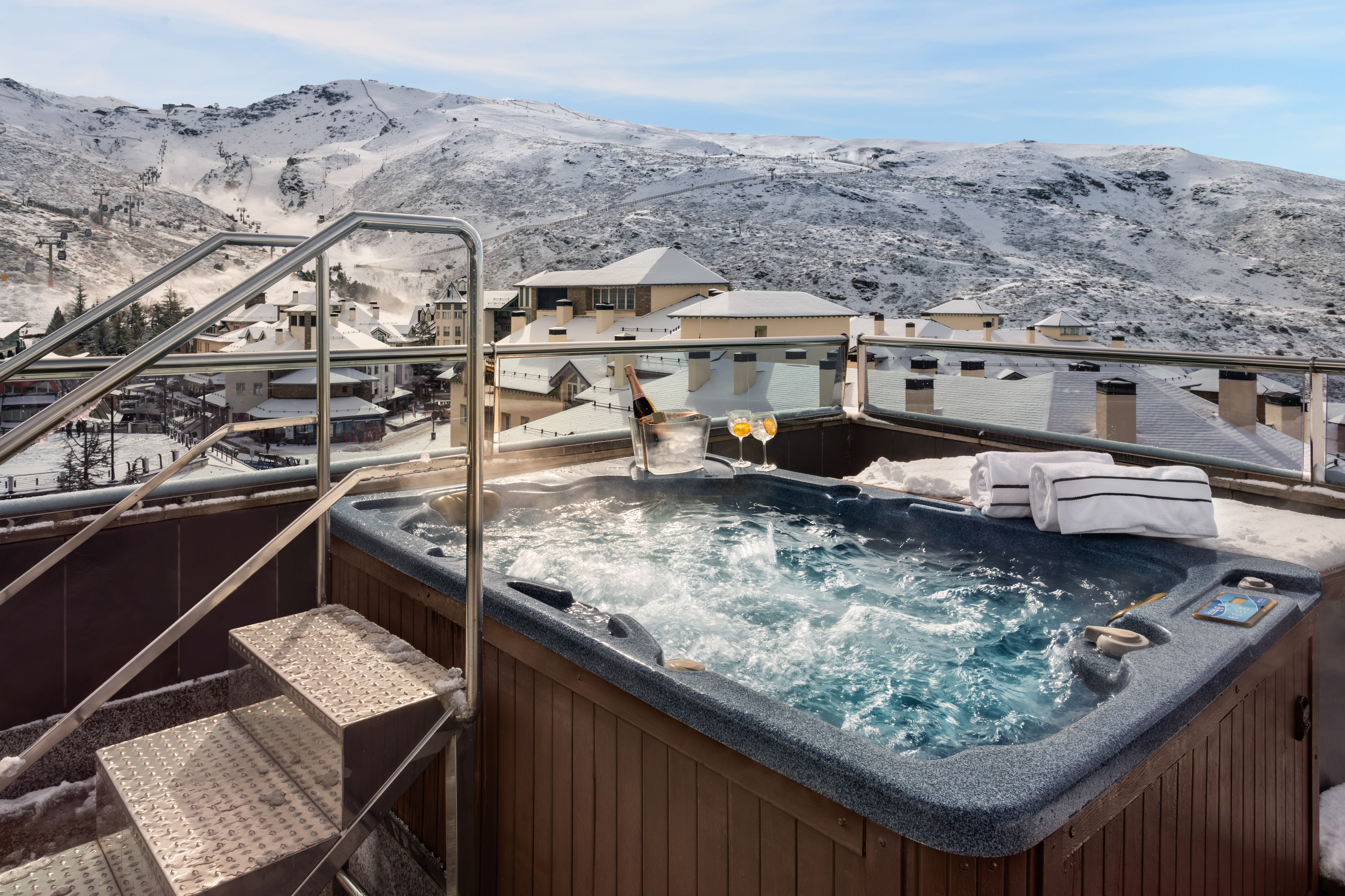 Bubbling outdoor hot tub with champagne, snowy ski resort view.