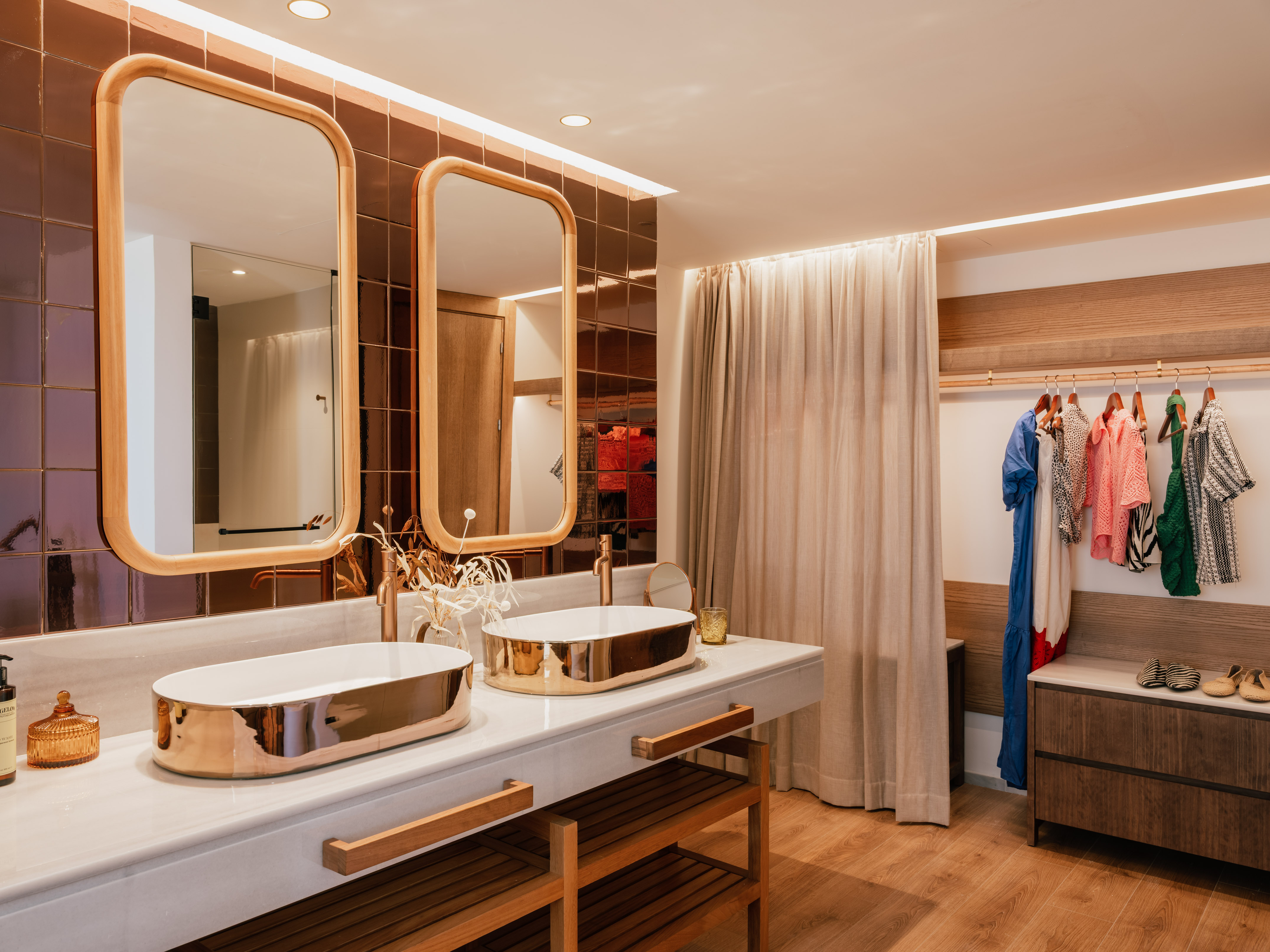 Modern double vanity with gold sinks, marble, wood mirrors, and clothes rack.
