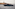 Dark blue luxury yacht cruising past a striped lighthouse on a rocky island.