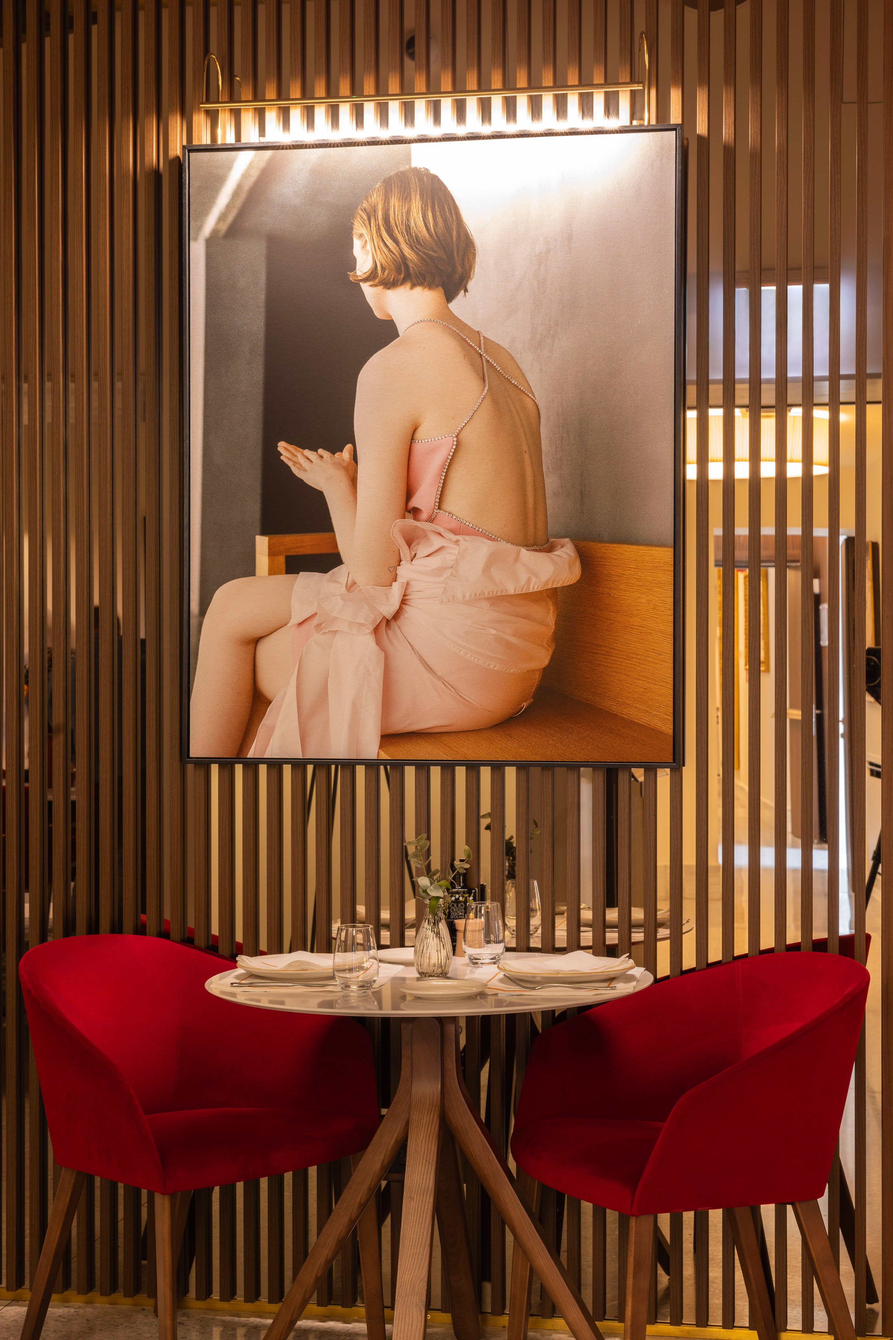 Restaurant interior: large artwork, red velvet chairs, and set dining table.