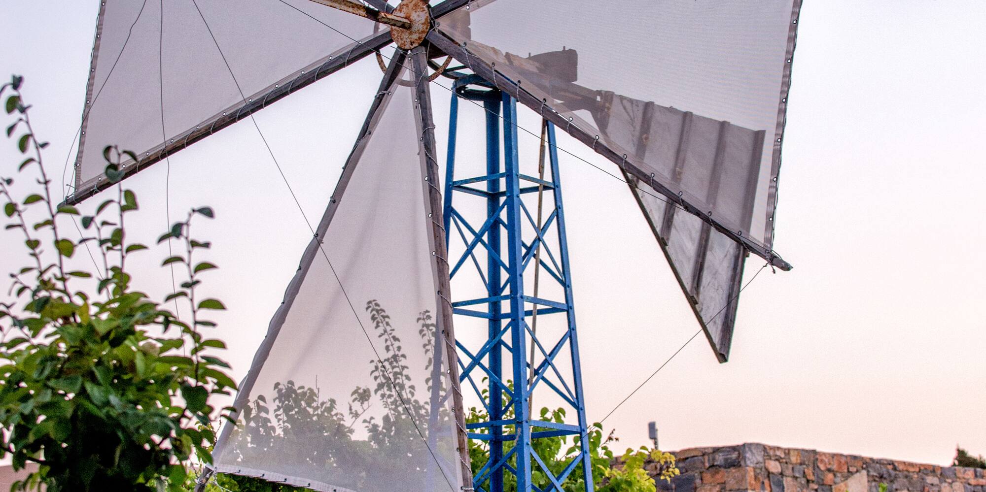 Cretan windmill with blue base and white sails in a green garden.