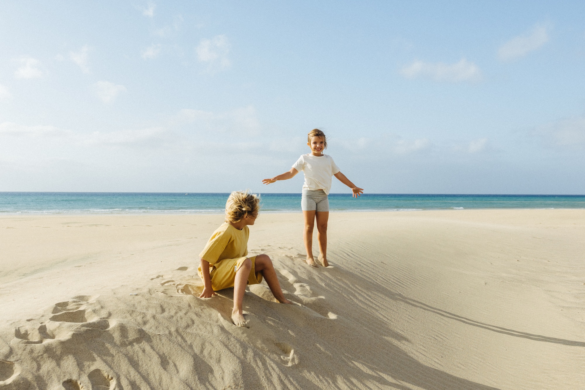 Niños jugando en dunas de arena en playa soleada con océano azul.