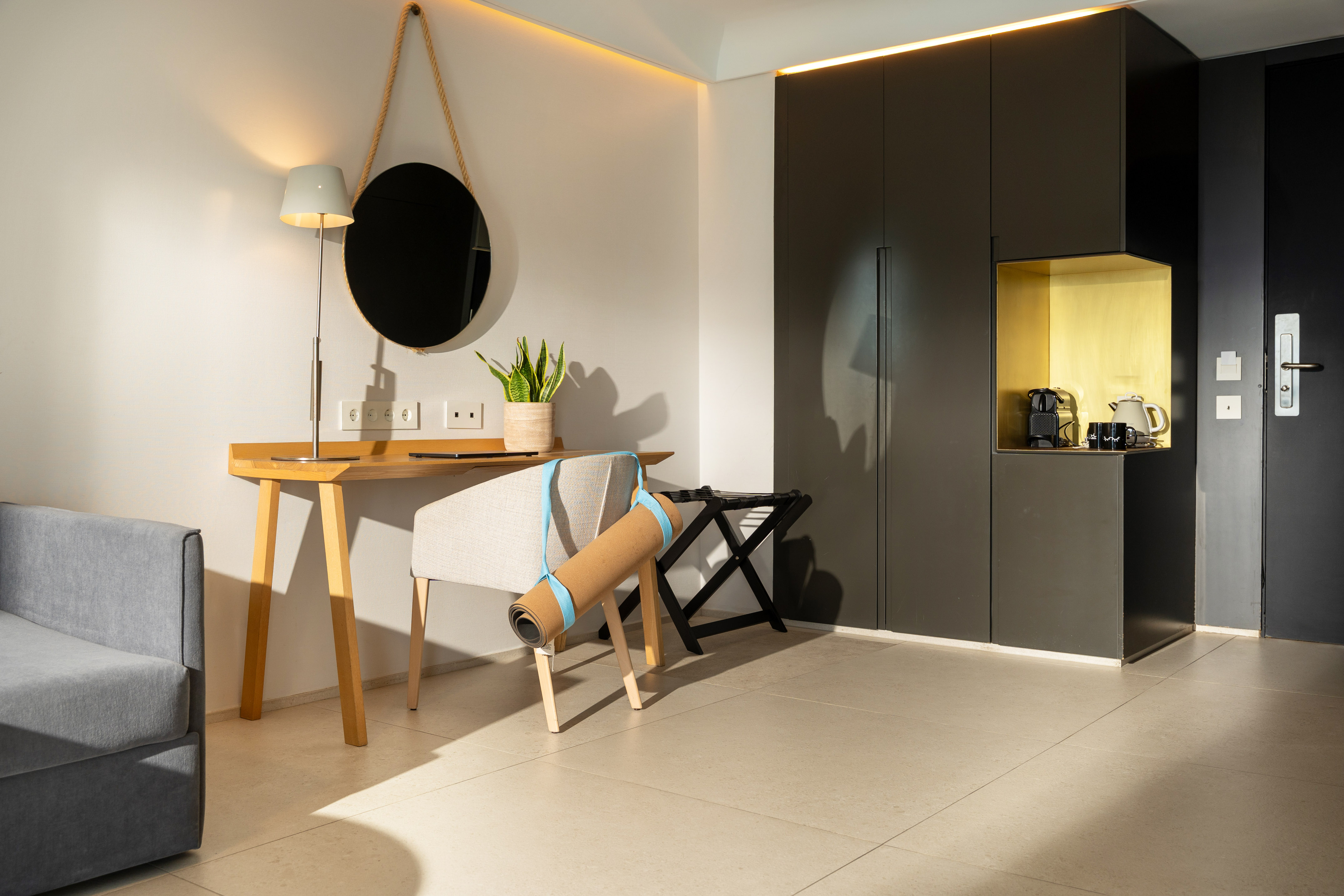 Modern hotel room with desk, coffee station, yoga mat, and gray sofa.