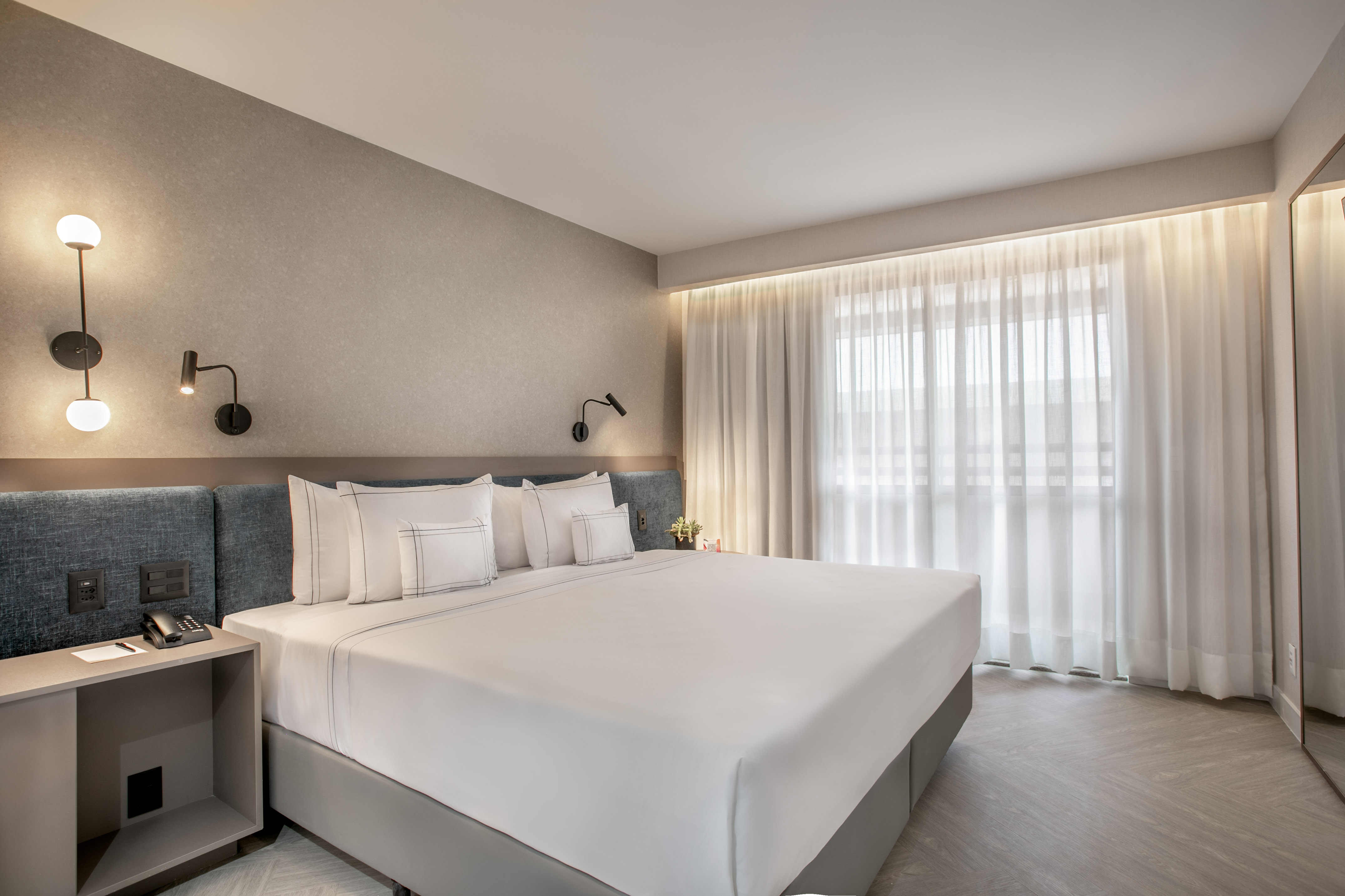 Modern hotel bedroom with king bed, white linens, and sheer window curtains.