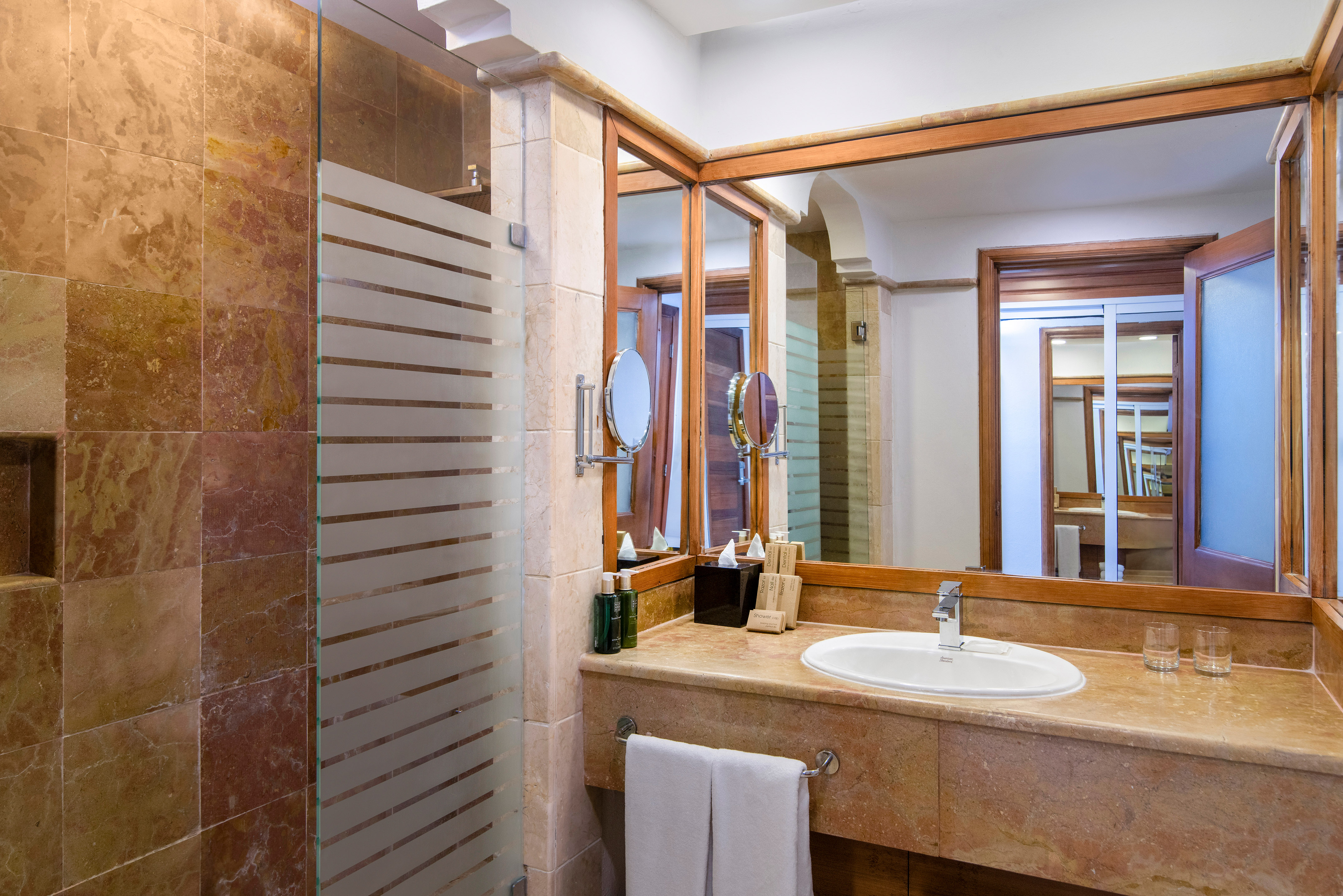 Travertine bathroom with white sink, large mirror, and frosted glass shower.