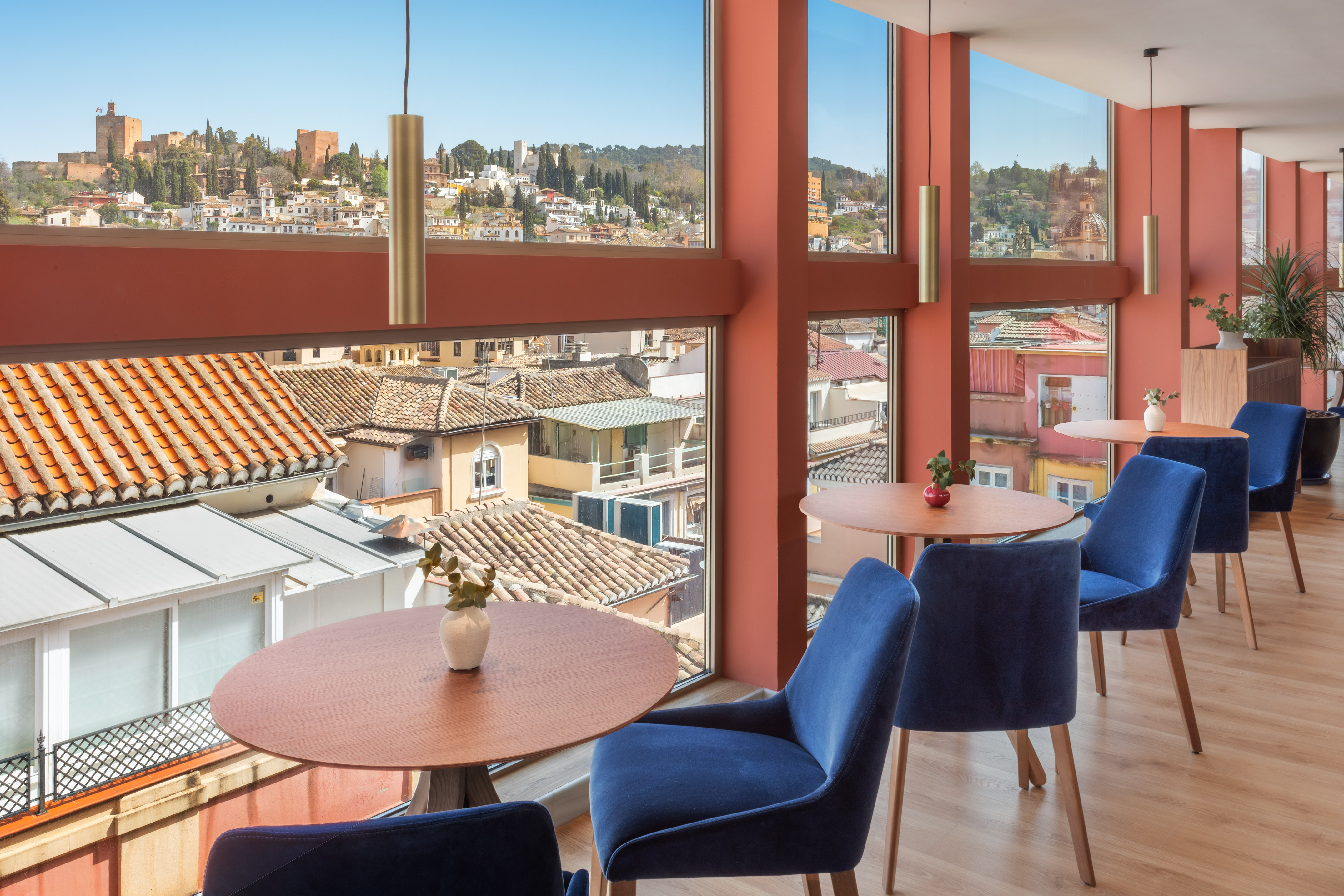 Modern cafe with panoramic Granada view, Alhambra, and blue chairs.