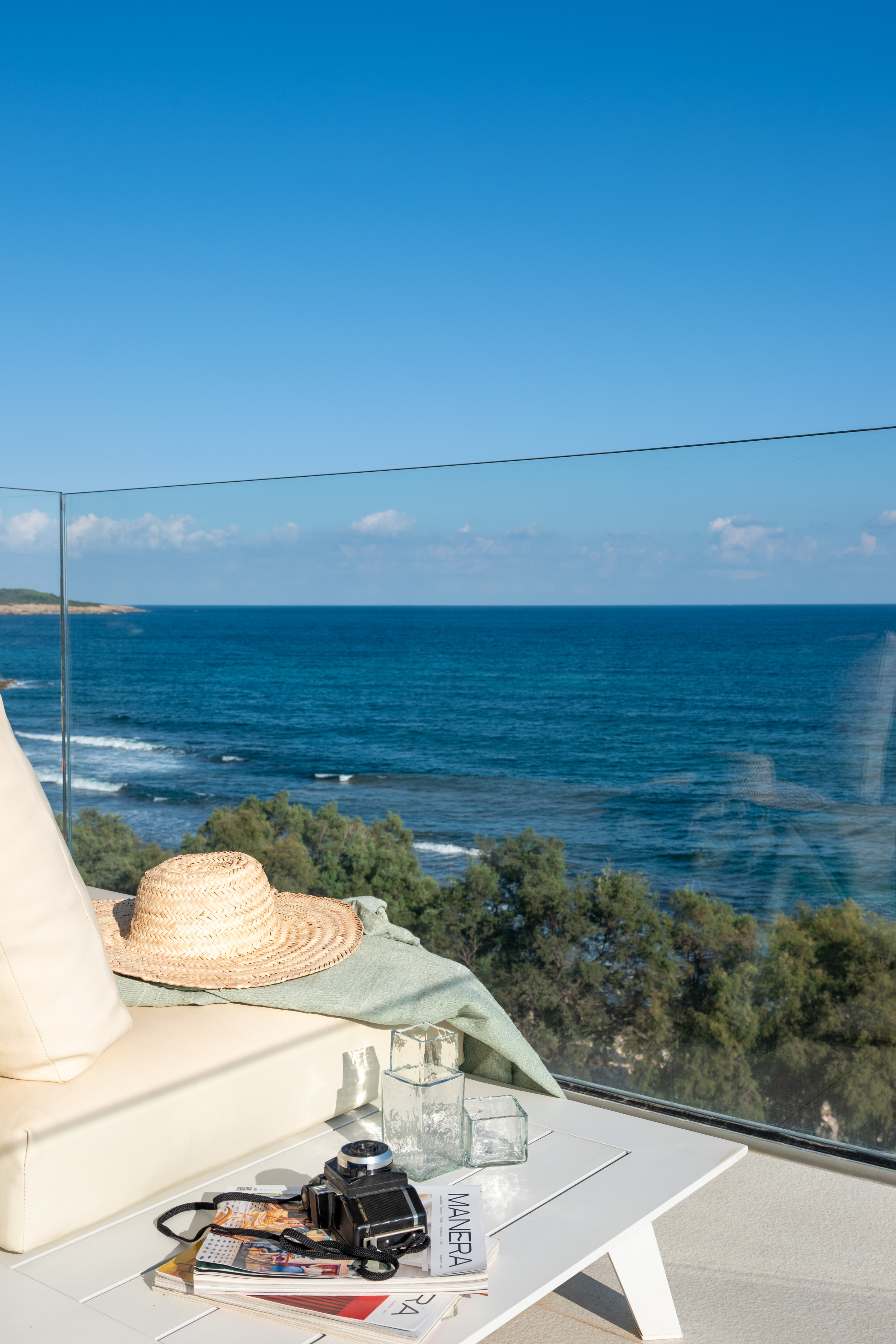 Balcony with ocean view, straw hat, camera, and magazines on a table.