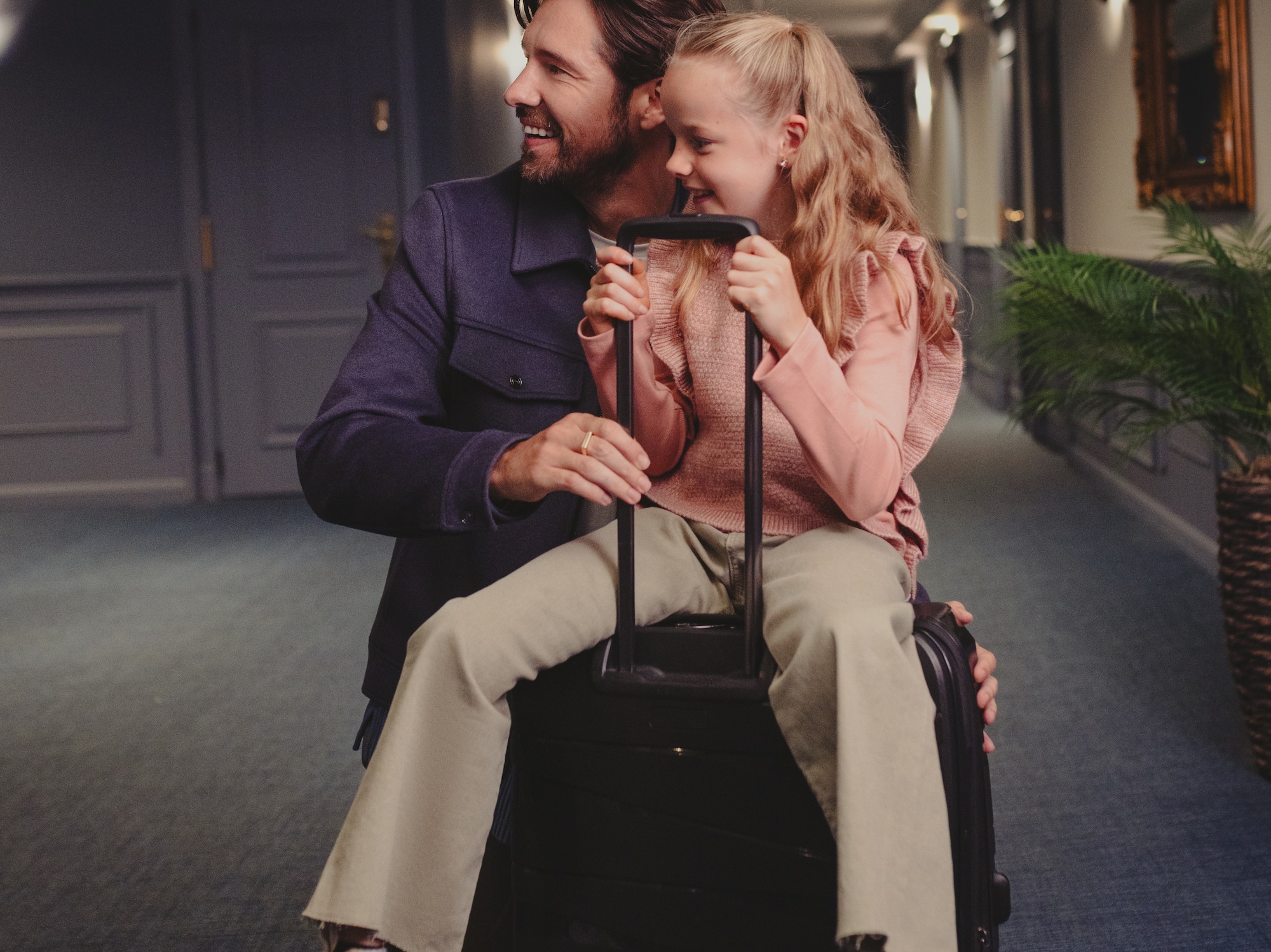a man and girl sitting on luggage in a hallway