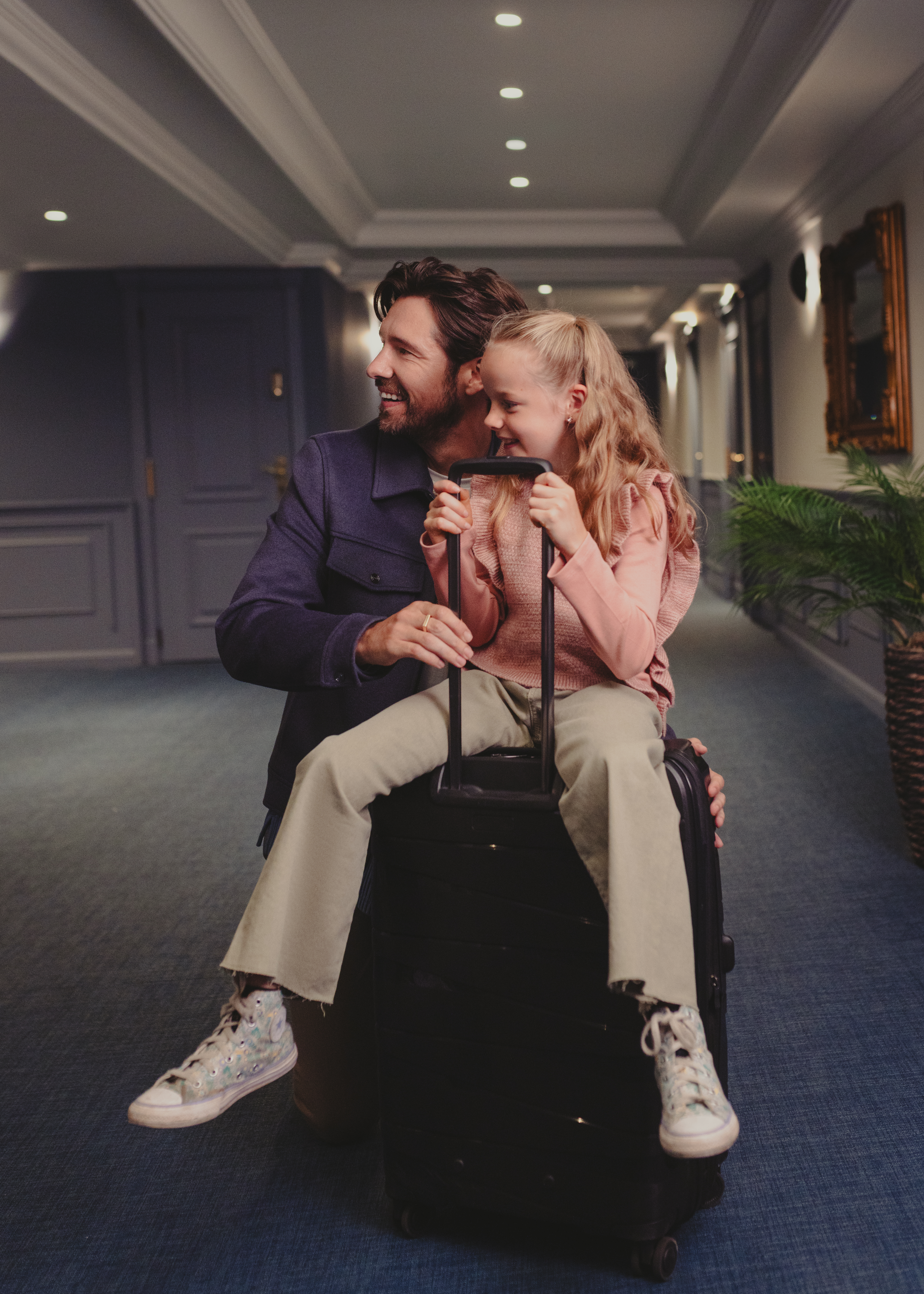 a man and girl sitting on luggage in a hallway