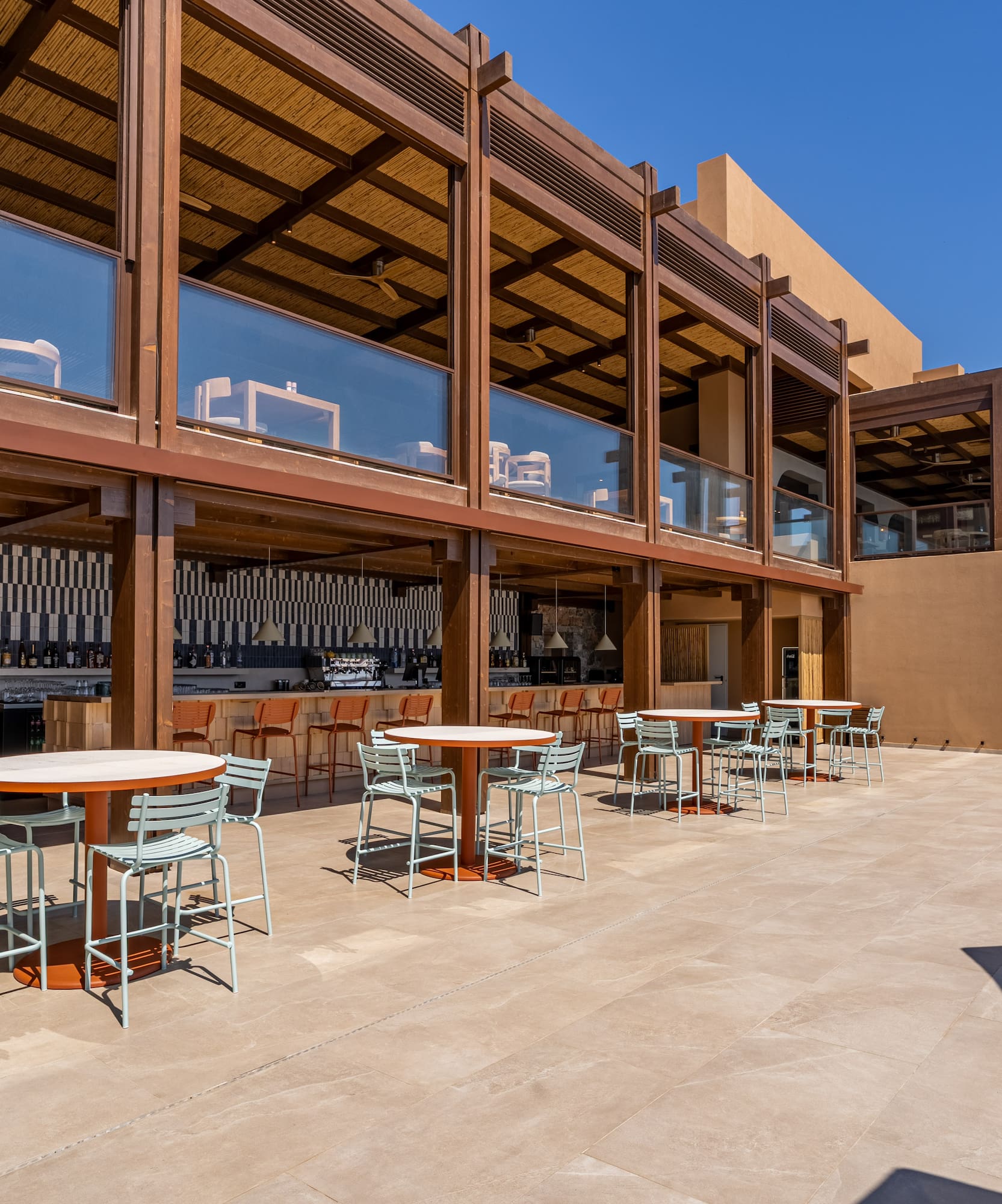 Modern resort outdoor patio and bar area with dining tables, wooden structure.