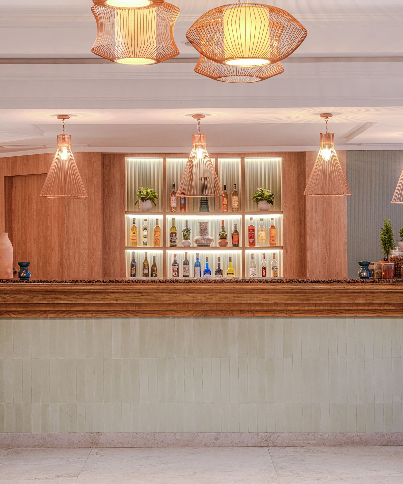 Bar de hotel moderno con estantes iluminados, bebidas y plantas decorativas.