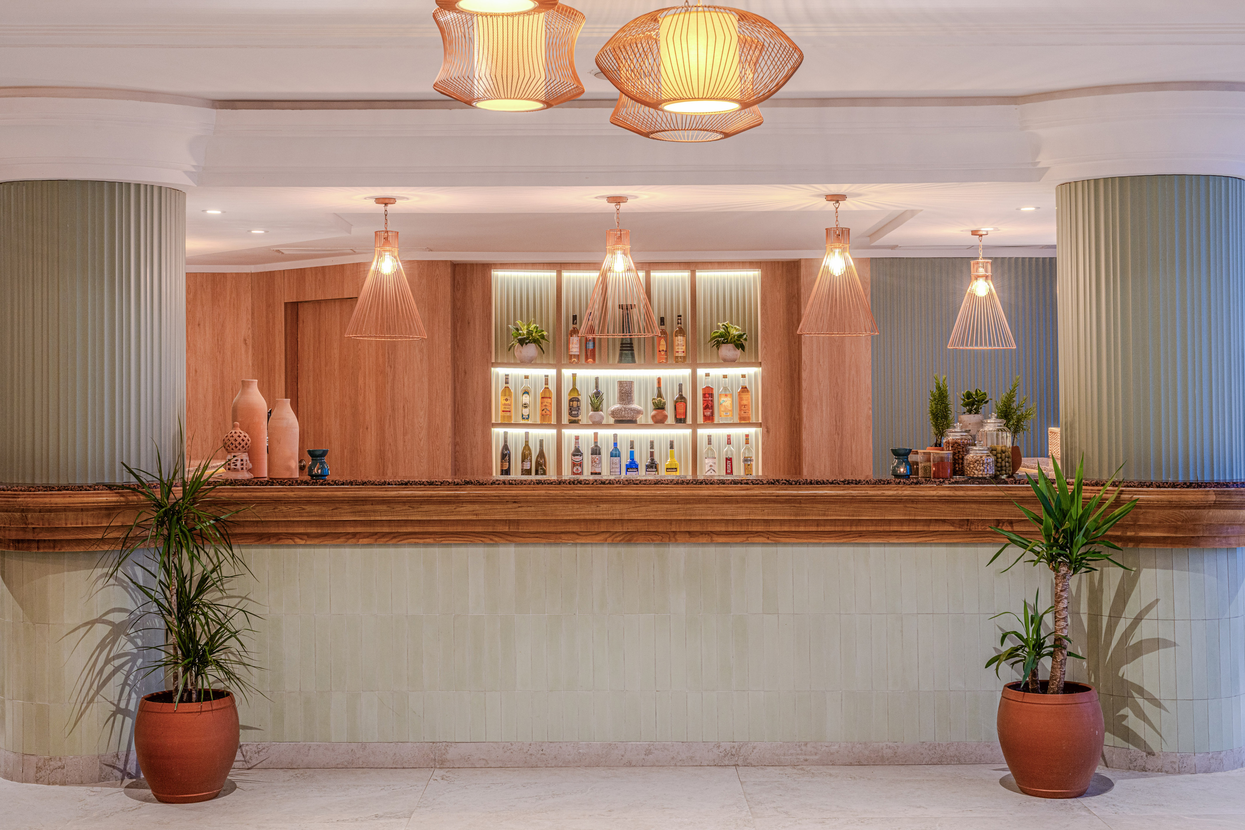 Bar de hotel moderno con estantes iluminados, bebidas y plantas decorativas.