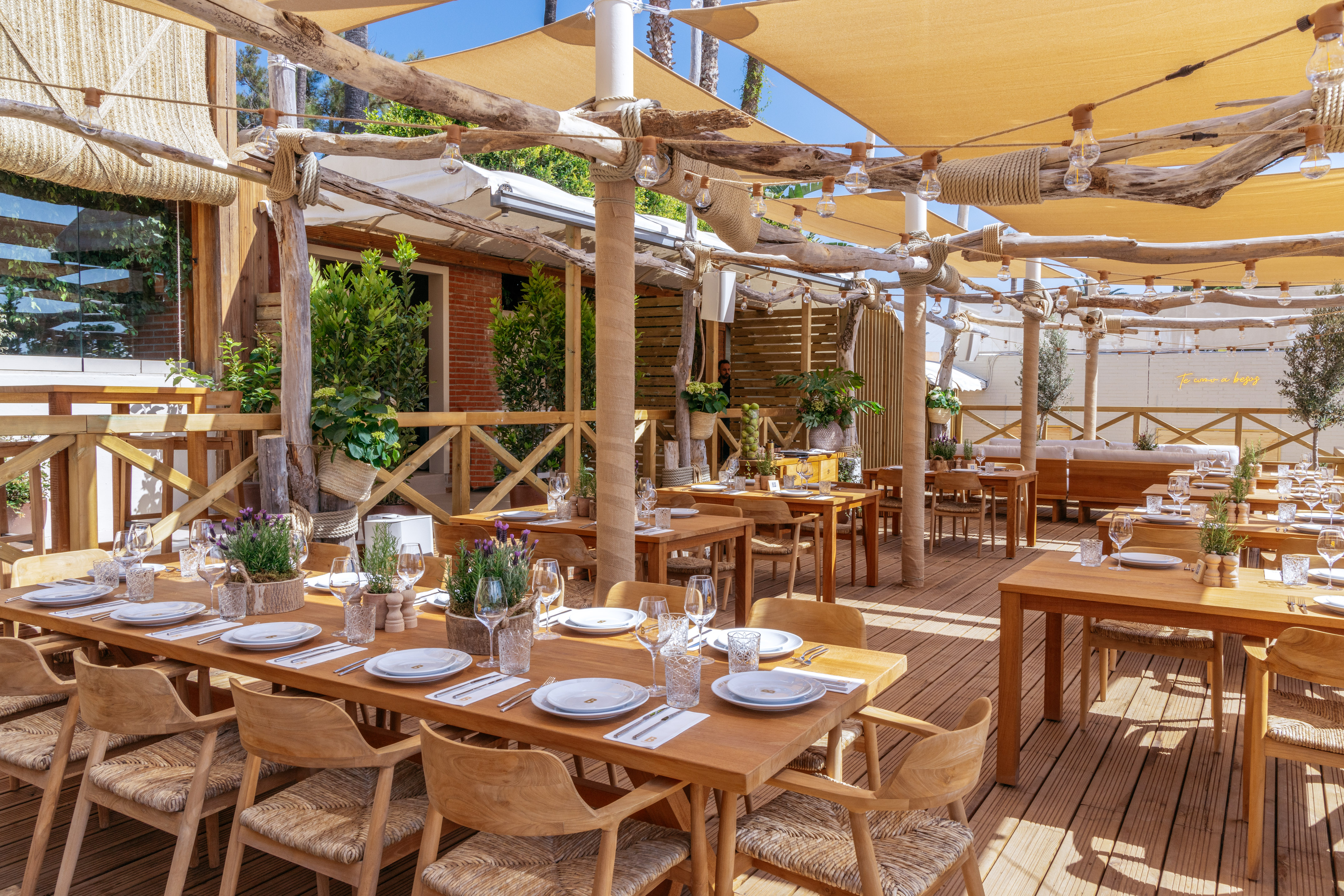 Outdoor restaurant patio with wooden tables, chairs, and sun canopy.
