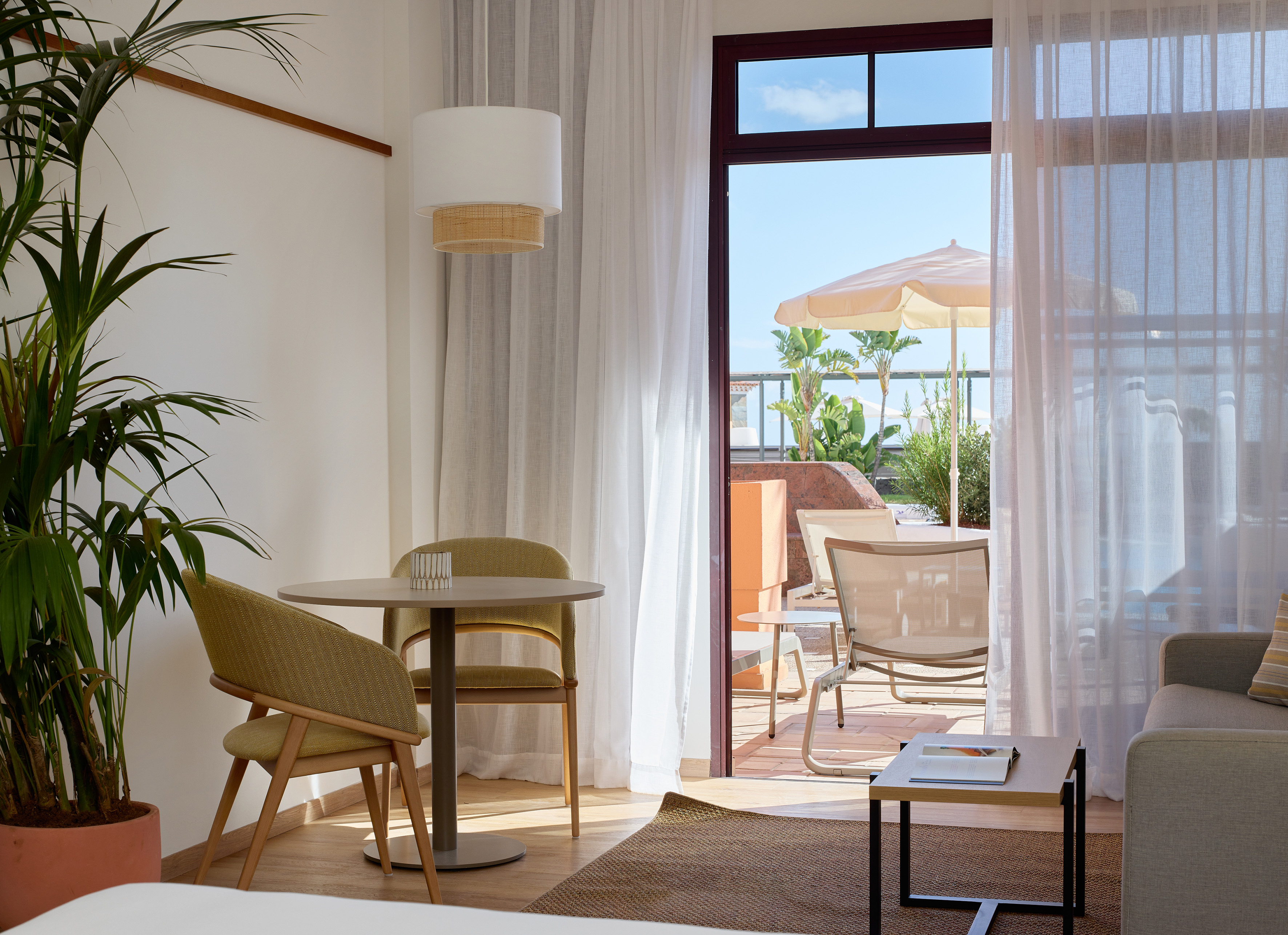 Bright hotel room with dining area, green plant, and sunny patio with umbrella.