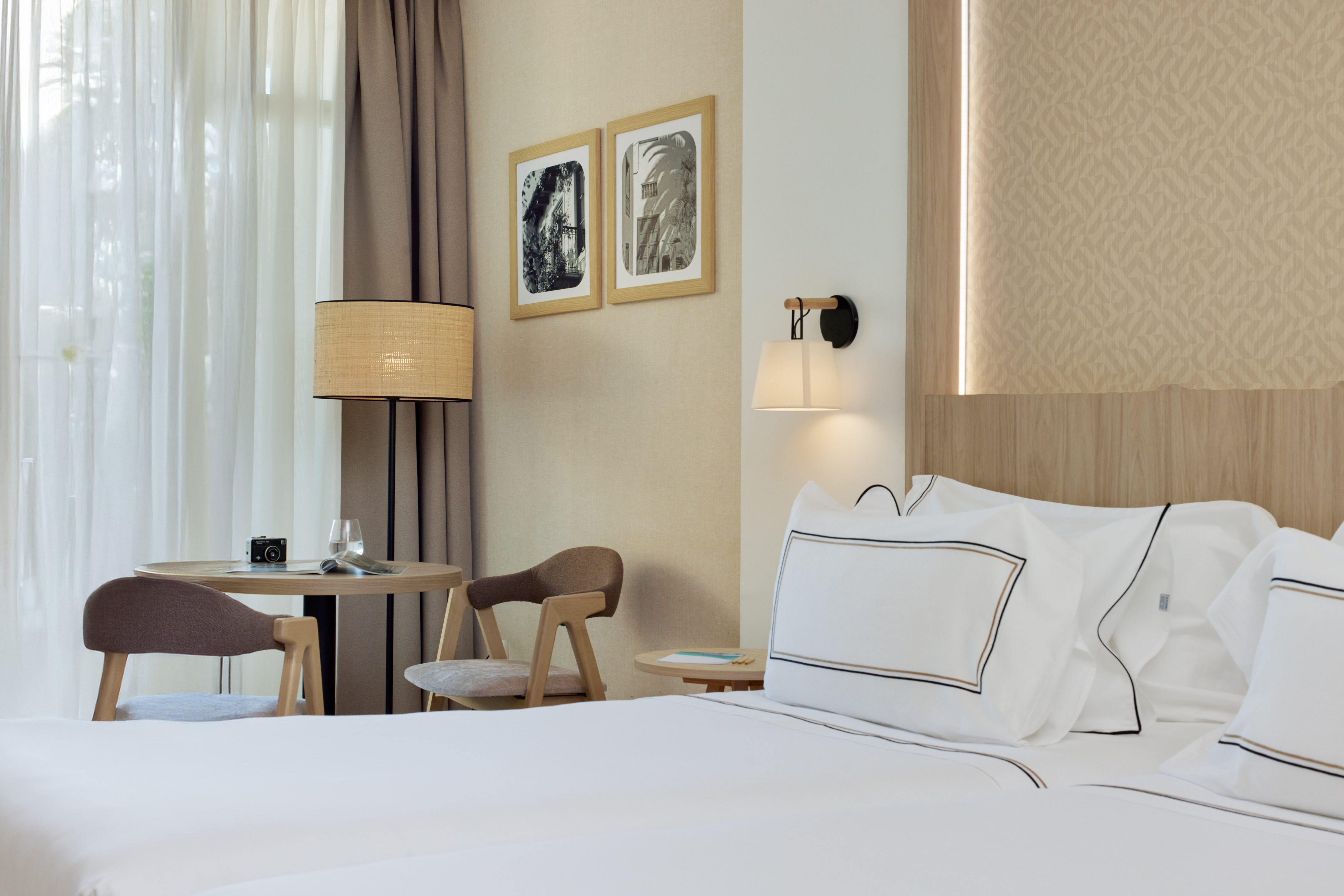 Bright hotel room with white bed, round table, chairs, and neutral decor.