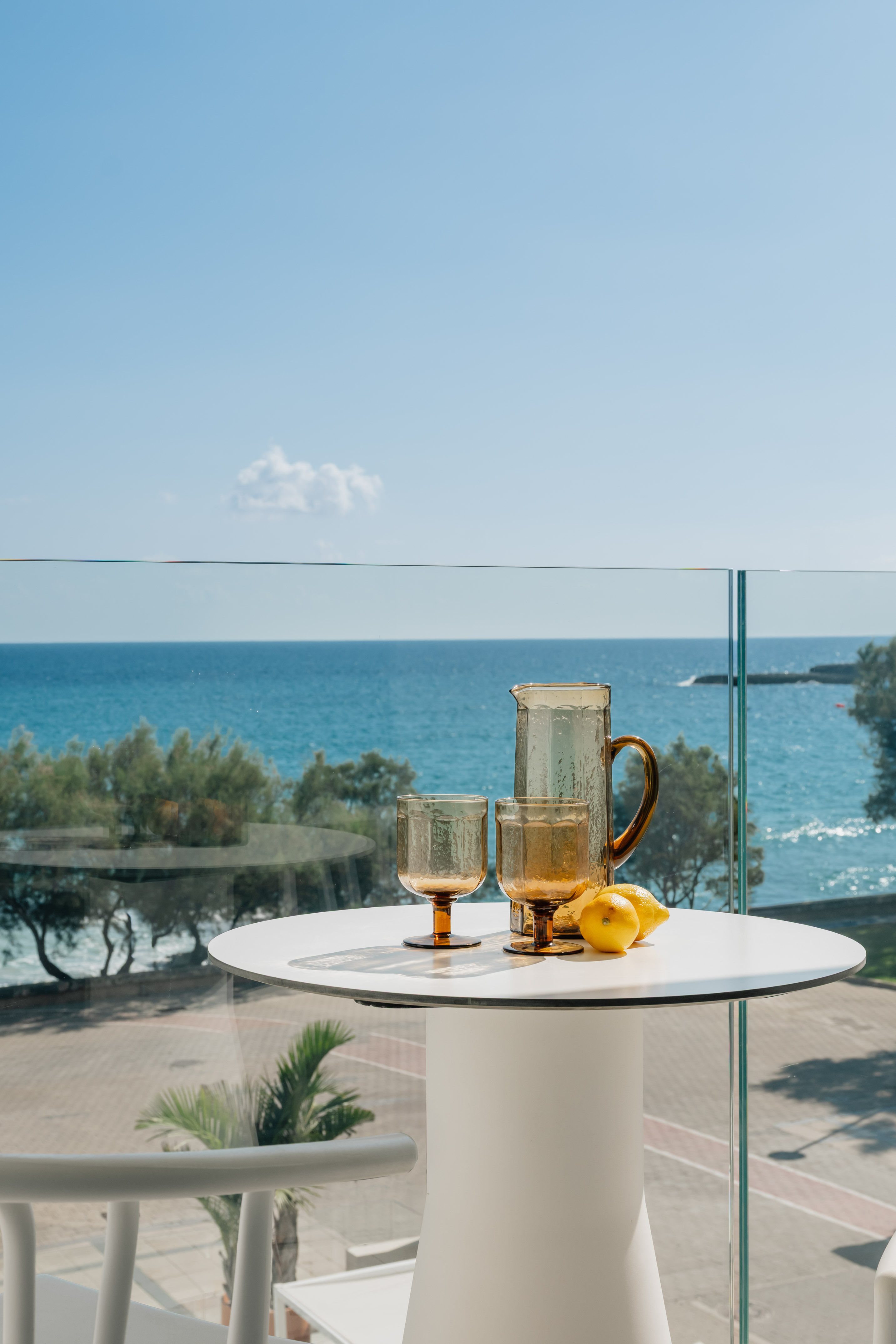 Amber pitcher, two glasses, lemons on a balcony table overlooking a blue ocean.