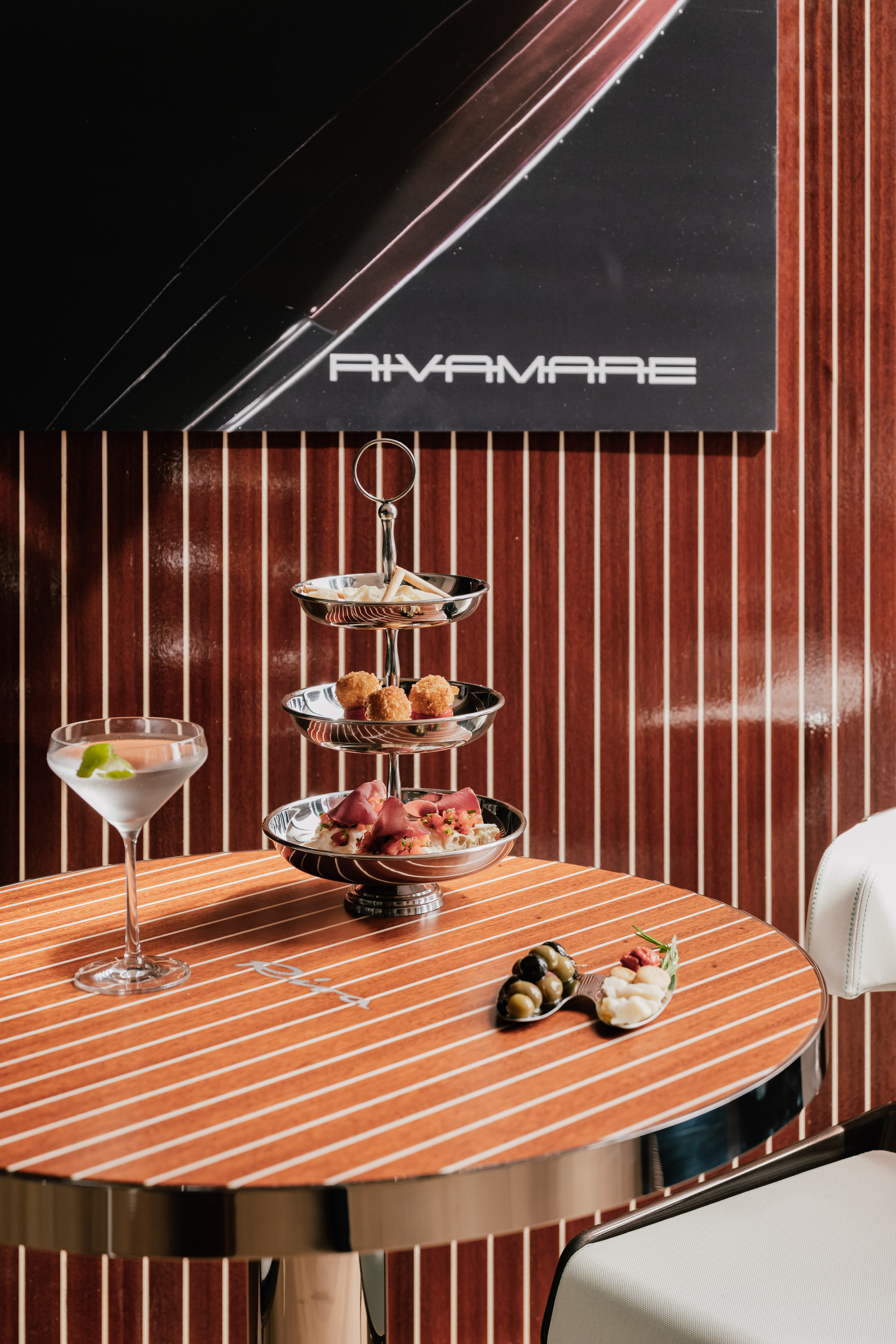Rivamare luxury bar with martini, tiered appetizers, and olives on a teak table.