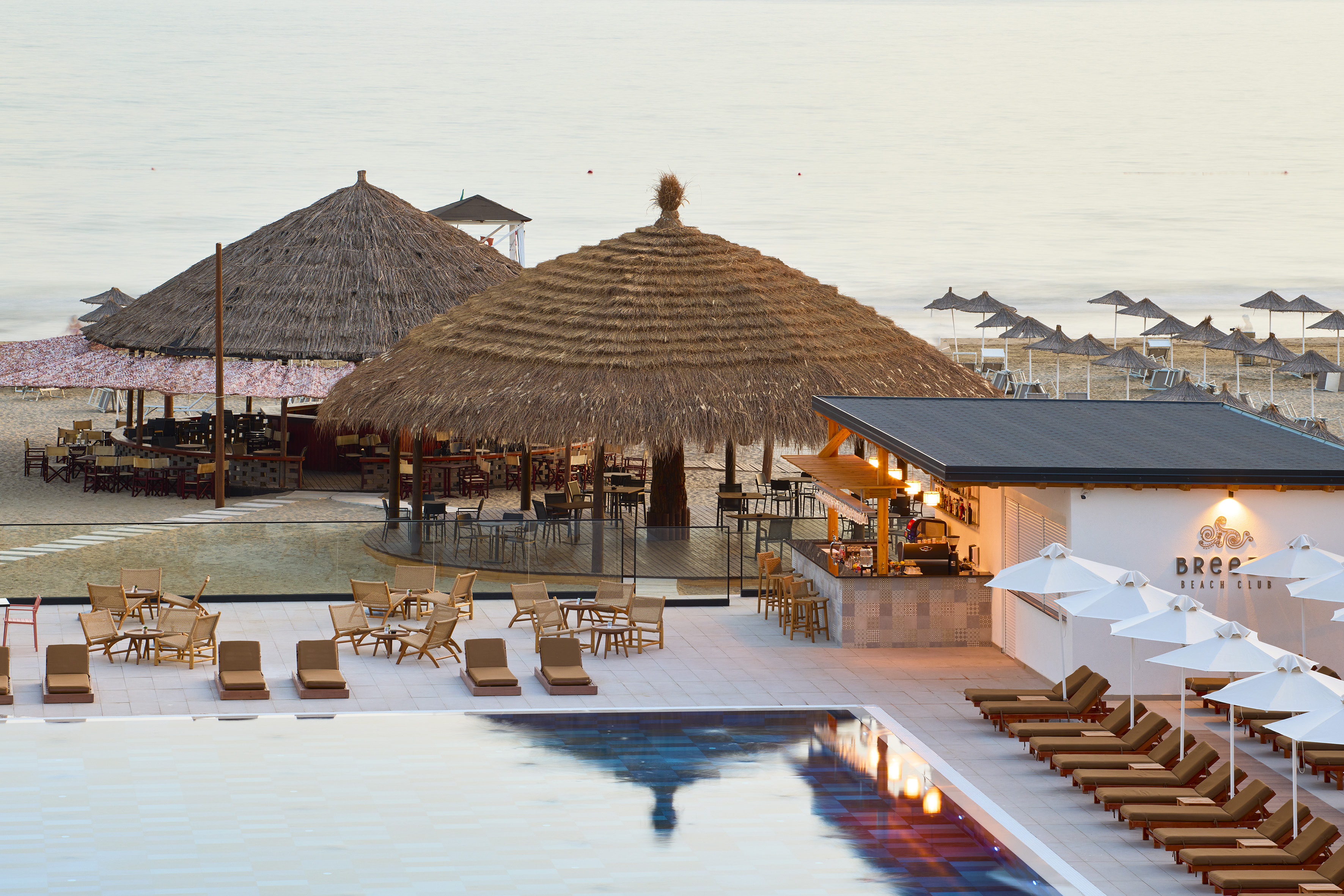 Breez Beach Club pool, thatched bars, beach, and ocean at dawn.