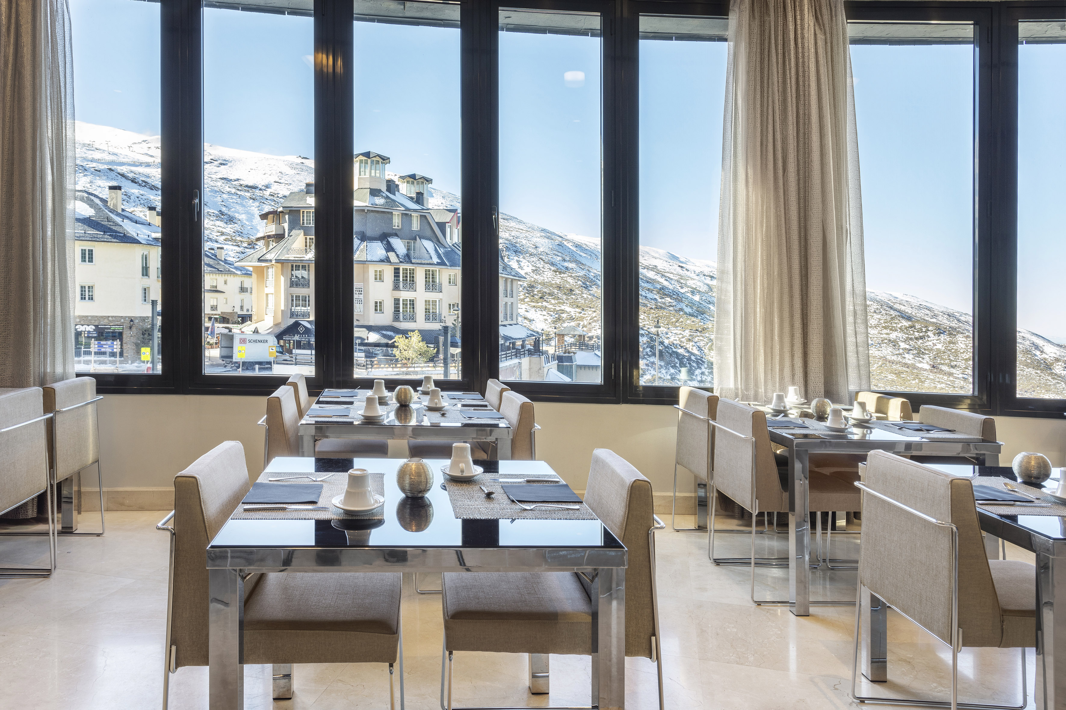 Modern restaurant with panoramic view of snowy mountains and a ski village.
