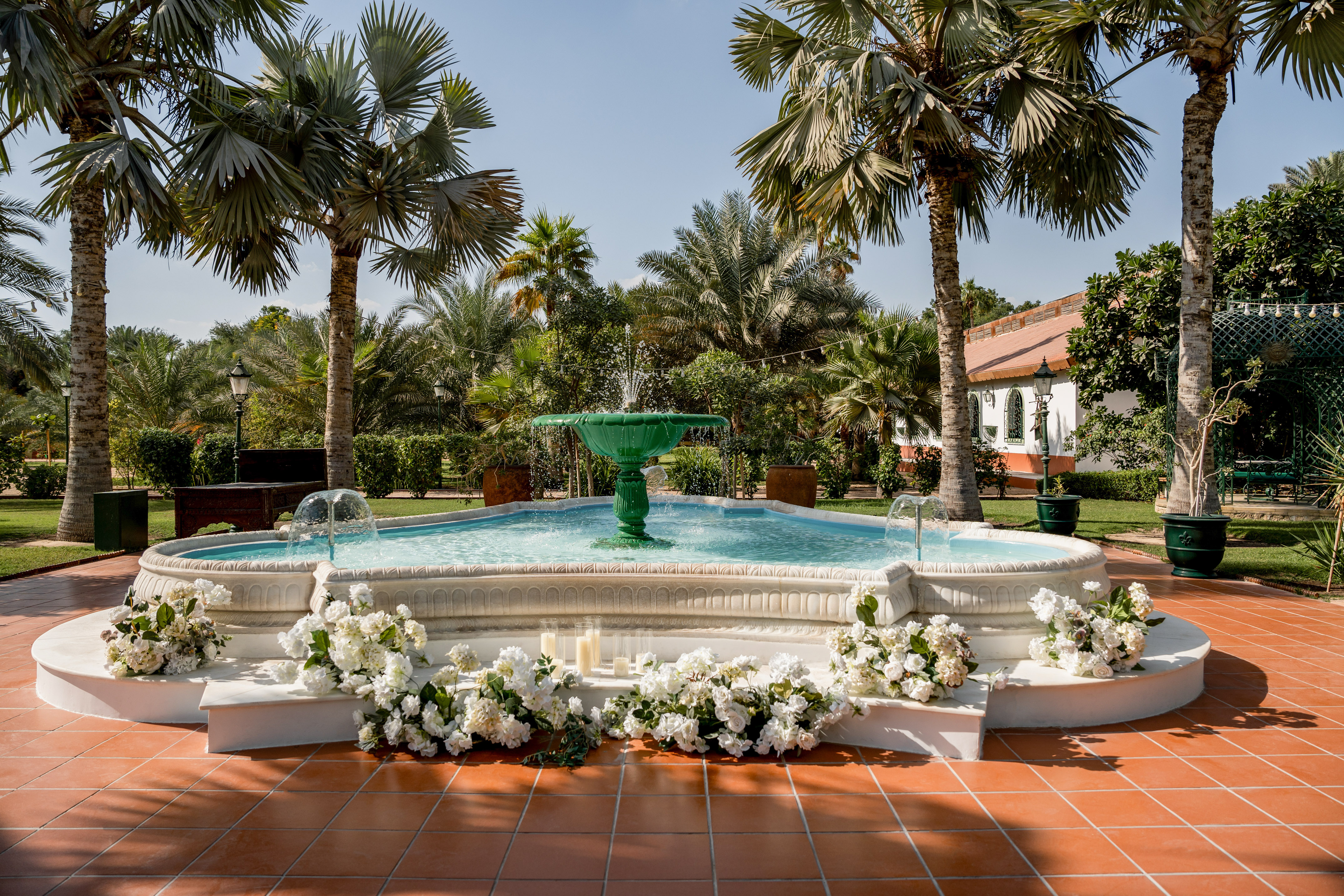 Tropical garden fountain decorated with white flowers and palm trees.