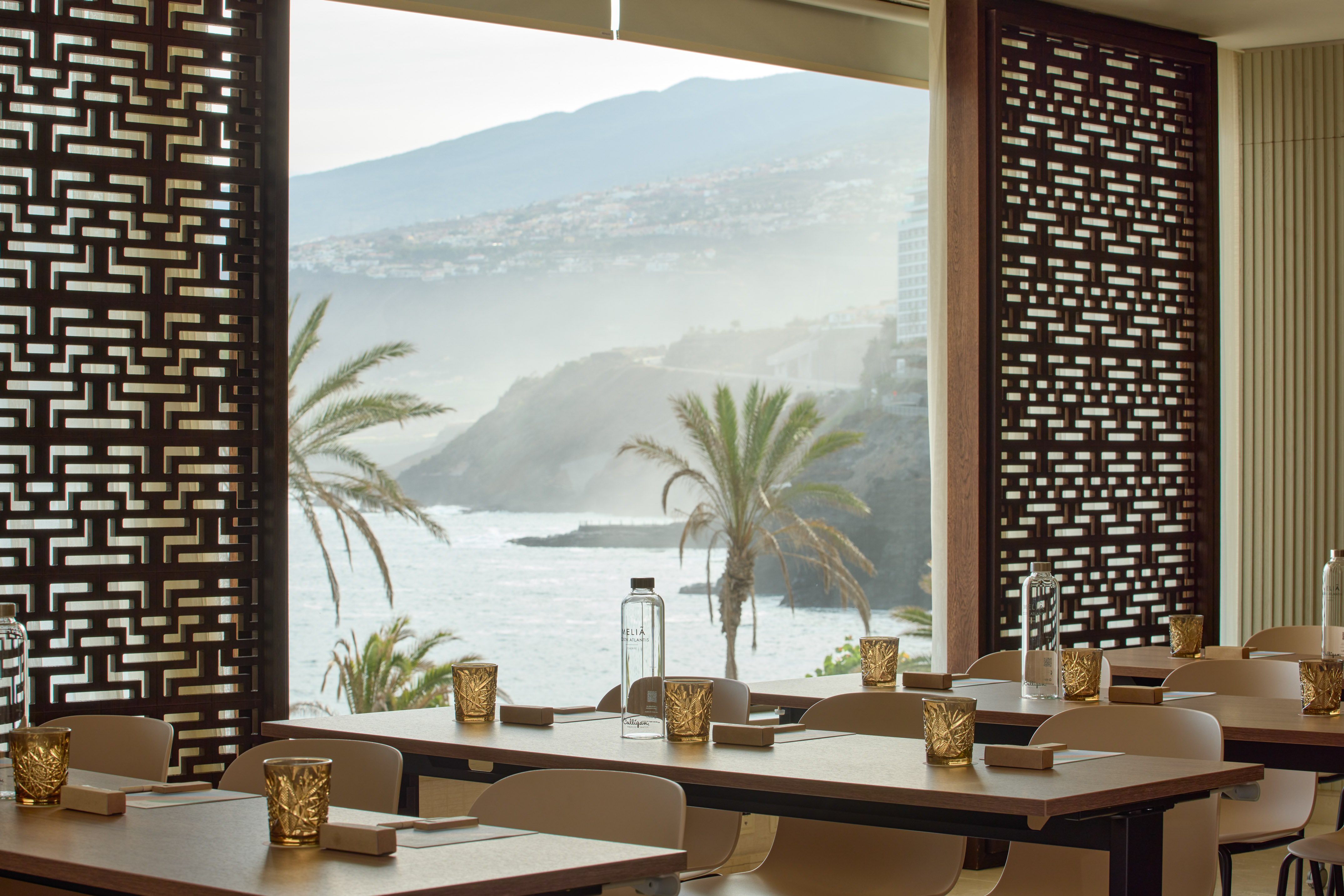 Coastal meeting room with ocean view, palm trees, and prepared tables.