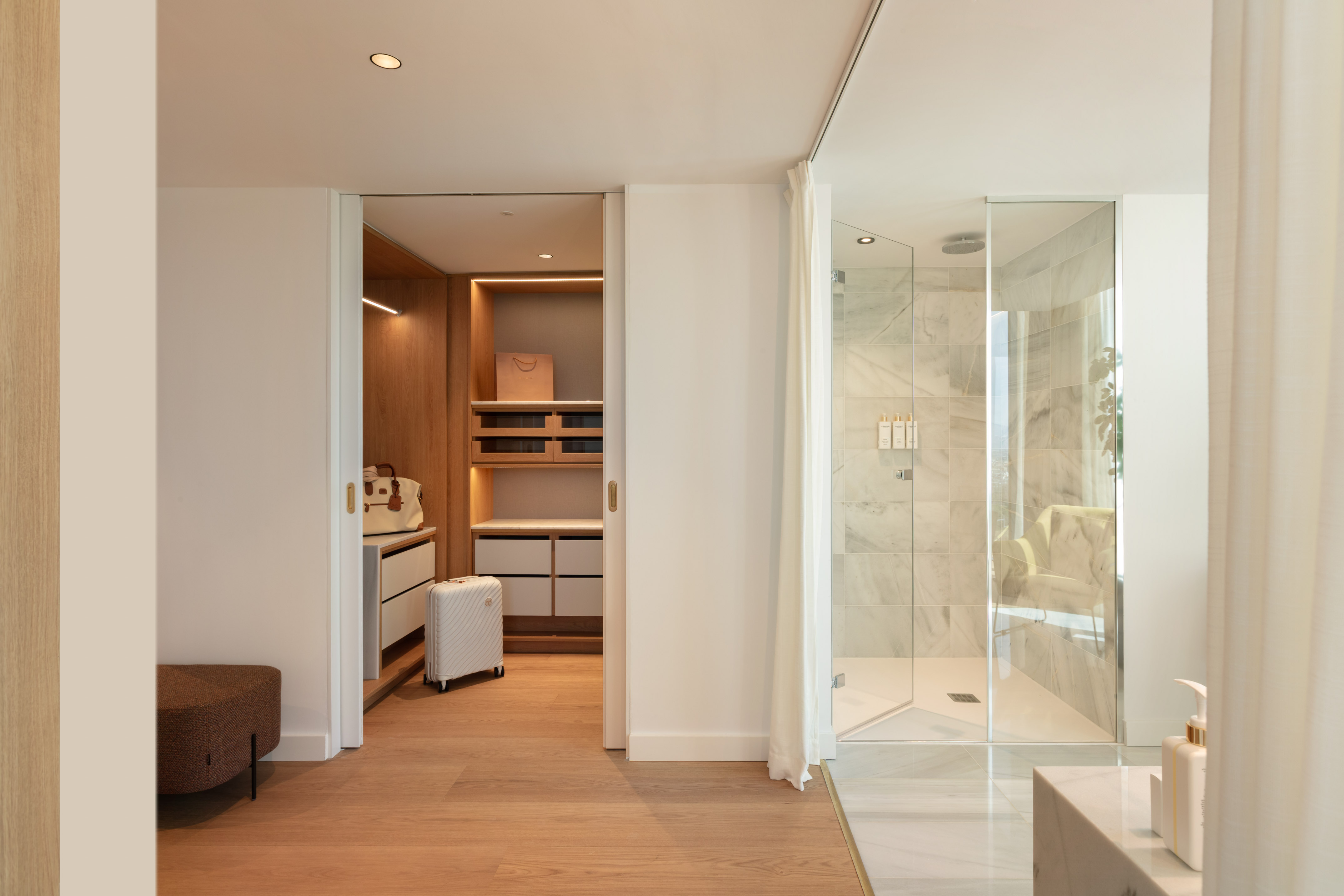 Modern wood walk-in closet and bright marble bathroom with glass shower.