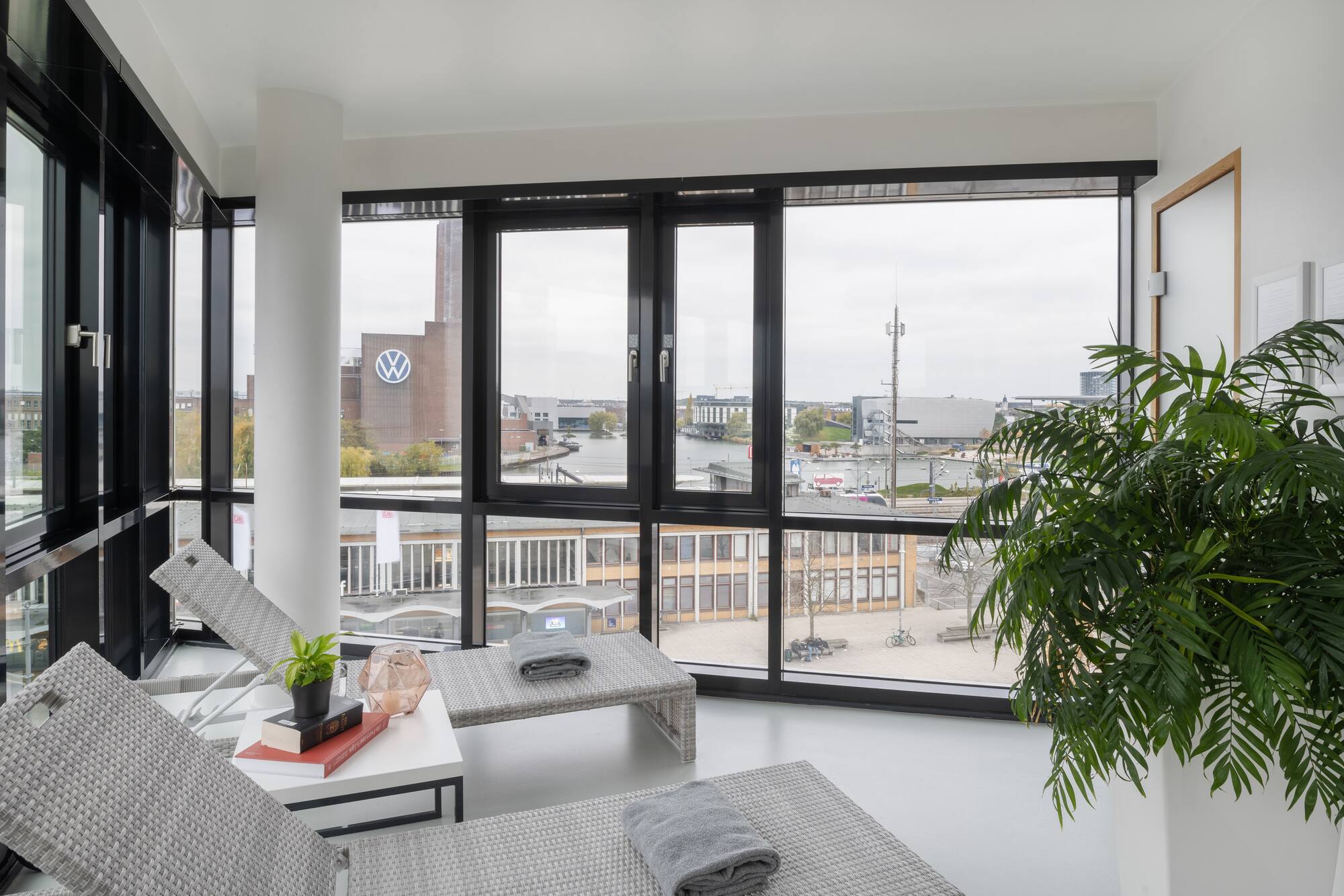 Lounge area with woven chairs, city view through large windows and VW building.