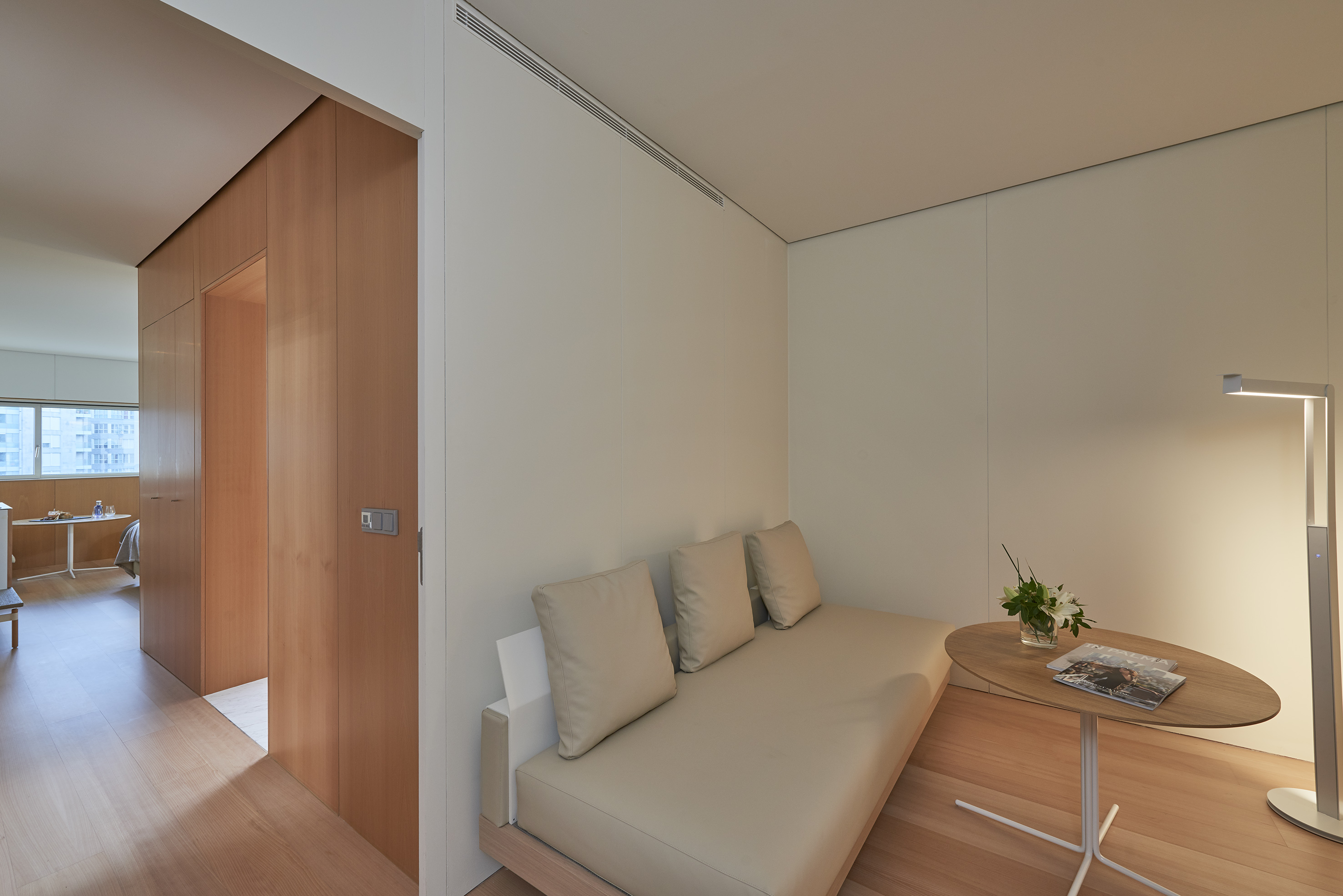 Minimalist living room with beige daybed, wooden floors, and modern lamp.