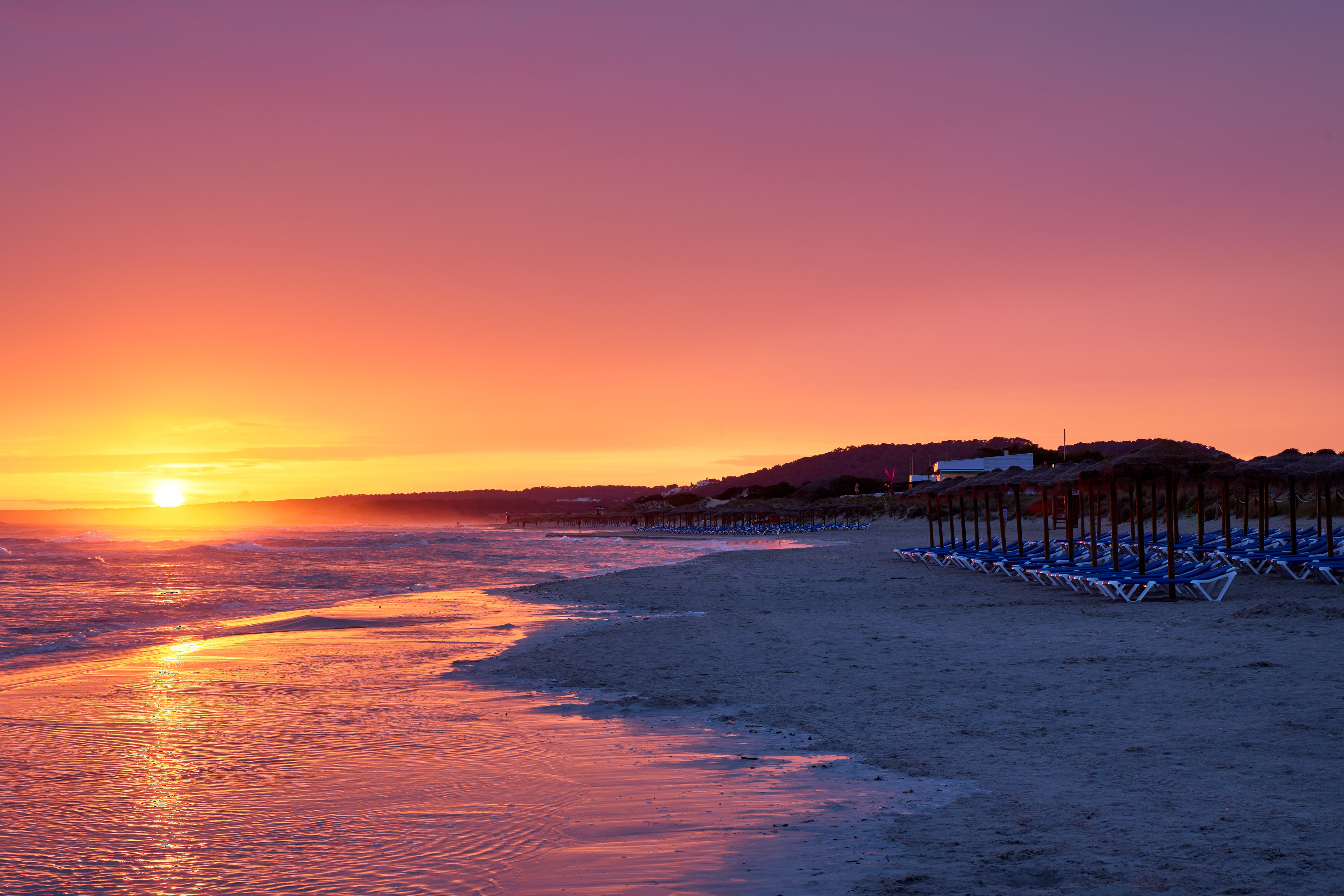 Vibrant sunset over beach with rows of umbrellas and lounge chairs.