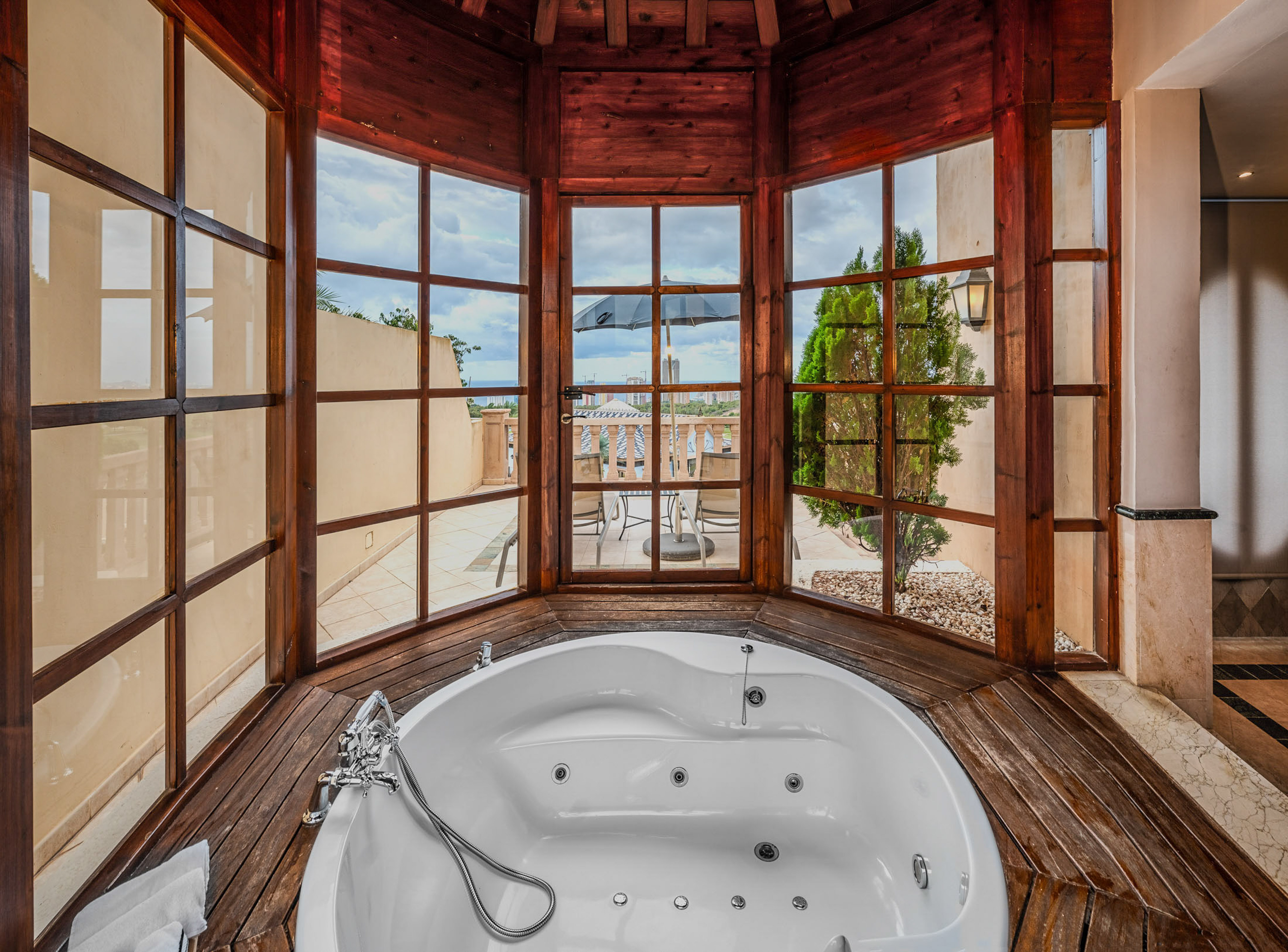 Luxury jacuzzi tub in wooden sunroom with panoramic balcony view.